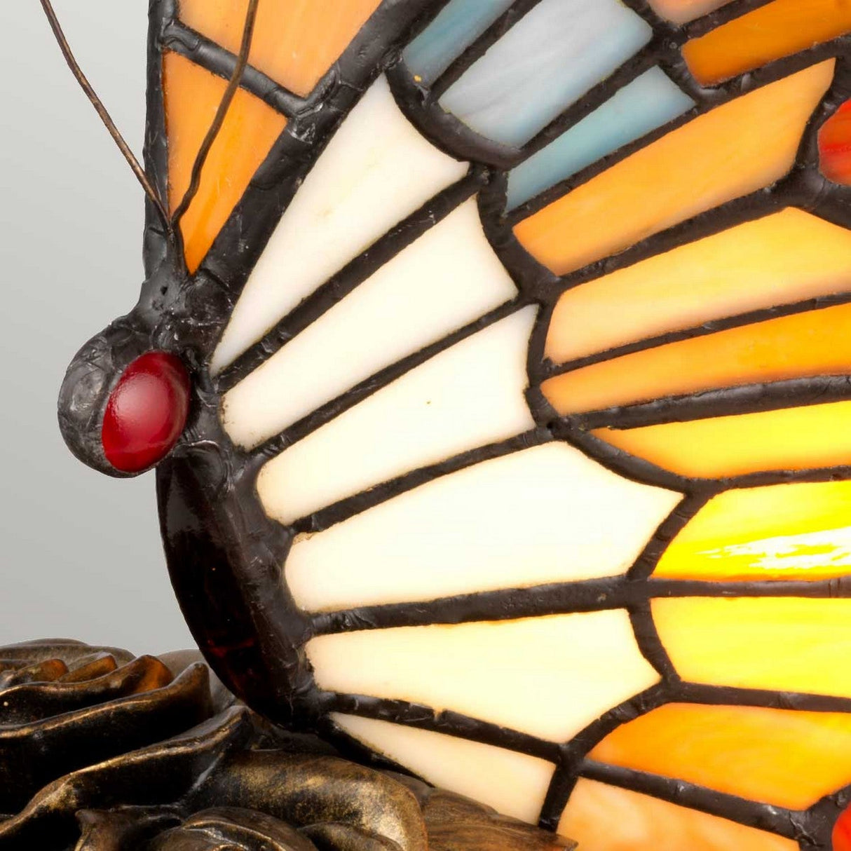 Close-up of the Tiffany Animal Lamps Orange Butterfly Lamp - Architectural Bronze, featuring a stained glass butterfly wing with vibrant orange, white, and black patterns enhanced by red accents. The architectural bronze base gracefully mimics the form of petals, accentuating its unique design.