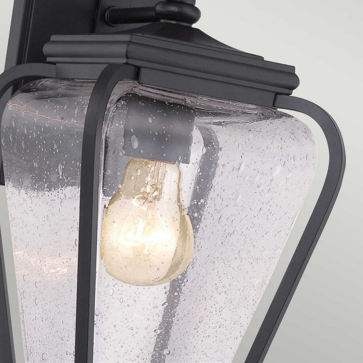 Close-up of the Province 1 Light Wall Lantern in black, featuring a cast aluminum frame and a clear seeded glass shade. The bubbled texture of the glass beautifully showcases the illuminated bulb within.