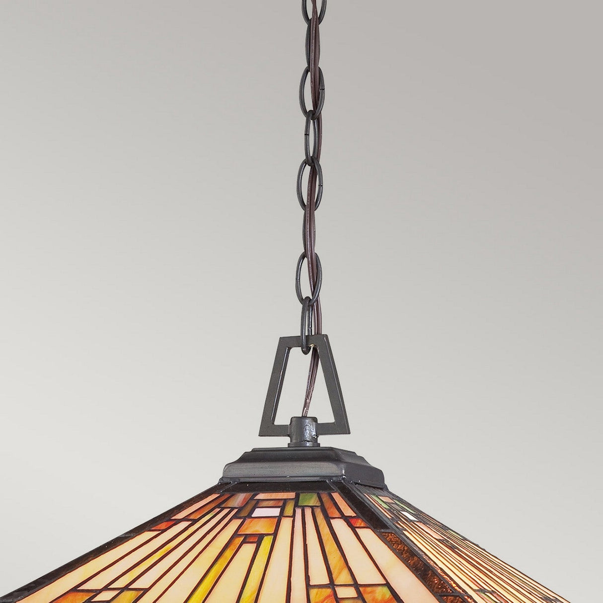 The Stephen 3 Light Tiffany Pendant - Vintage Bronze showcases a beautifully crafted stained glass shade adorned with a geometric pattern in rich shades of orange, yellow, and brown. Hanging from a vintage bronze chain, its design captures the essence of Arts & Crafts style, making it an eye-catching centerpiece for any room.