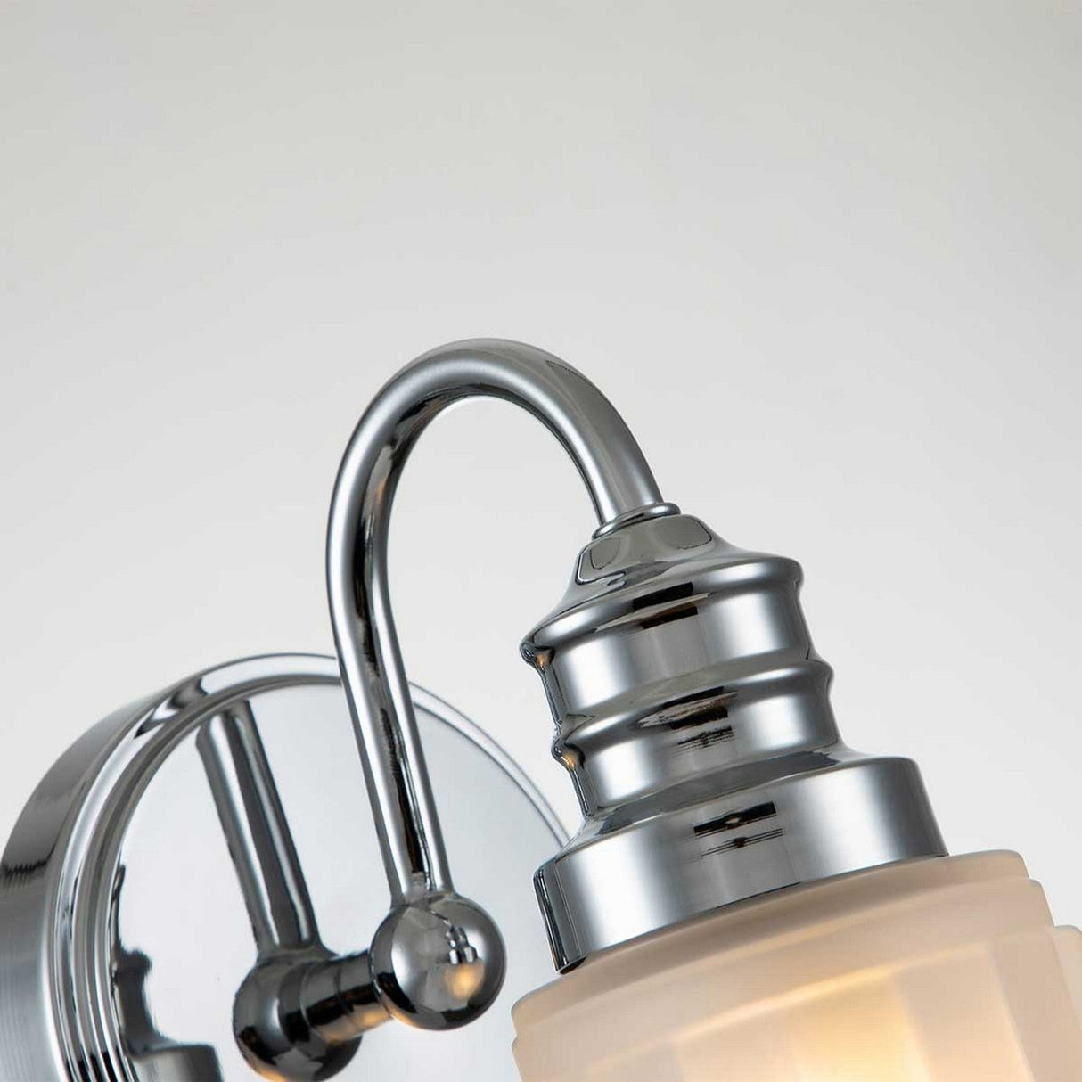 Here's a close-up of the Swell 1 Light Wall Light - Polished Chrome, showcasing its contemporary polished chrome finish with a gracefully curved arm and frosted glass shade. The fixture is installed on a round base and casts a gentle illumination, complemented by a neutral backdrop. Ideal for areas where an IP44 rating is essential.
