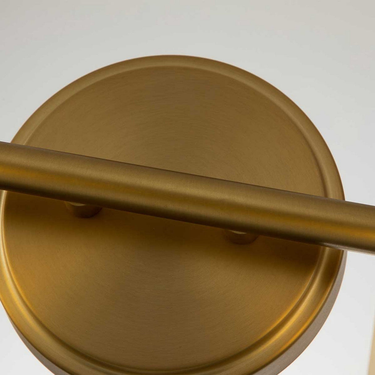 The Swell 2 Light Wall Light in brushed brass showcases an industrial aesthetic with its round, bronze-colored metal form and diagonally positioned cylindrical bar. Its brushed brass texture provides a matte finish, characteristic of refined wall lights with an IP44 rating.