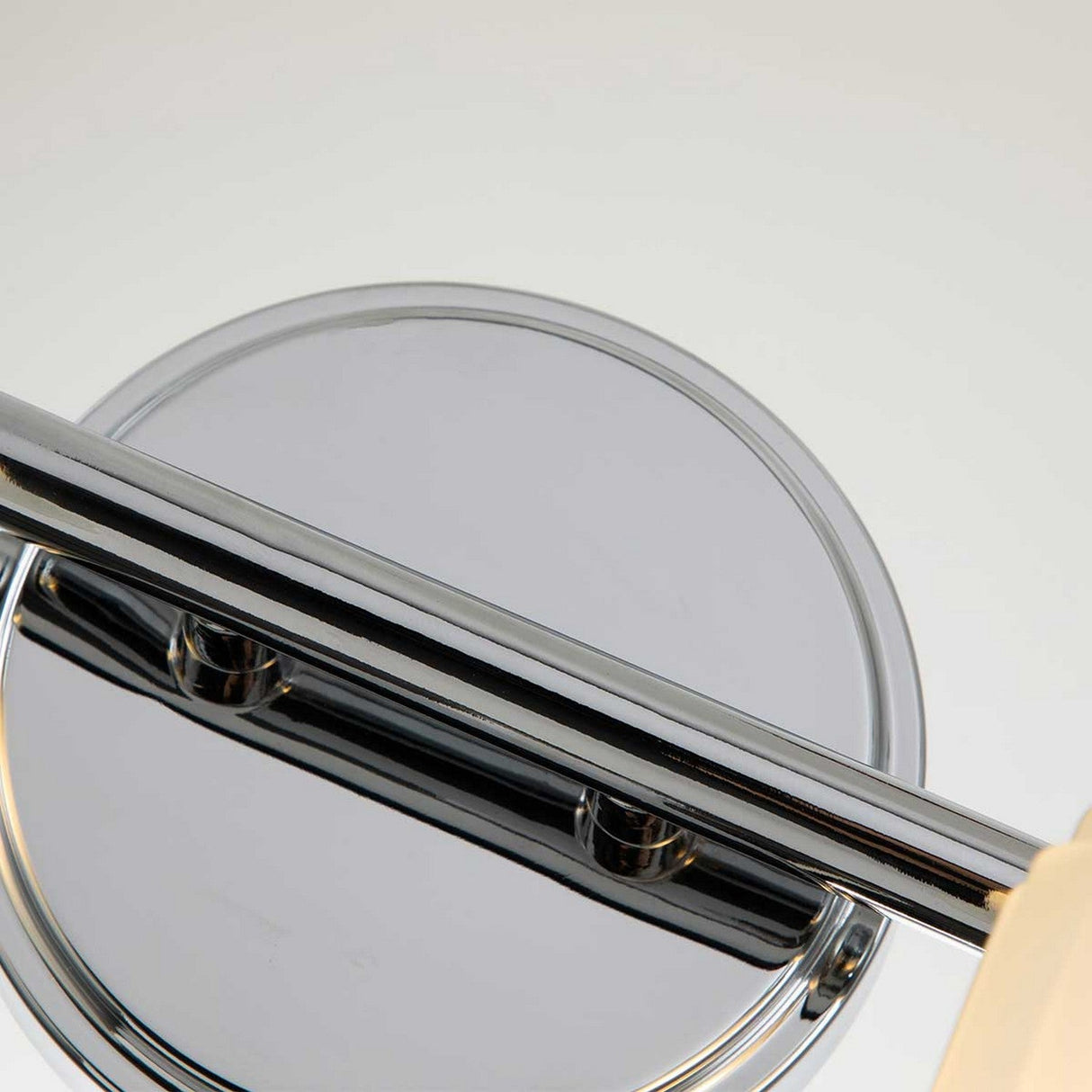 Close-up of a polished chrome wall-mounted magnifying mirror with a circular design, featuring a swiveling arm for adjustable positioning. The Swell 2 Light Wall Light in polished chrome complements the fixture perfectly, adding a touch of elegance against a light background.