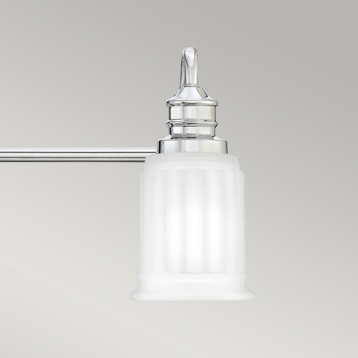 The Swell 3 Light Wall Light in Polished Chrome features a frosted white glass shade designed to resemble a classical column, making it the ideal choice for enhancing bathroom vanities. It casts a gentle, ambient light against the plain light gray background.