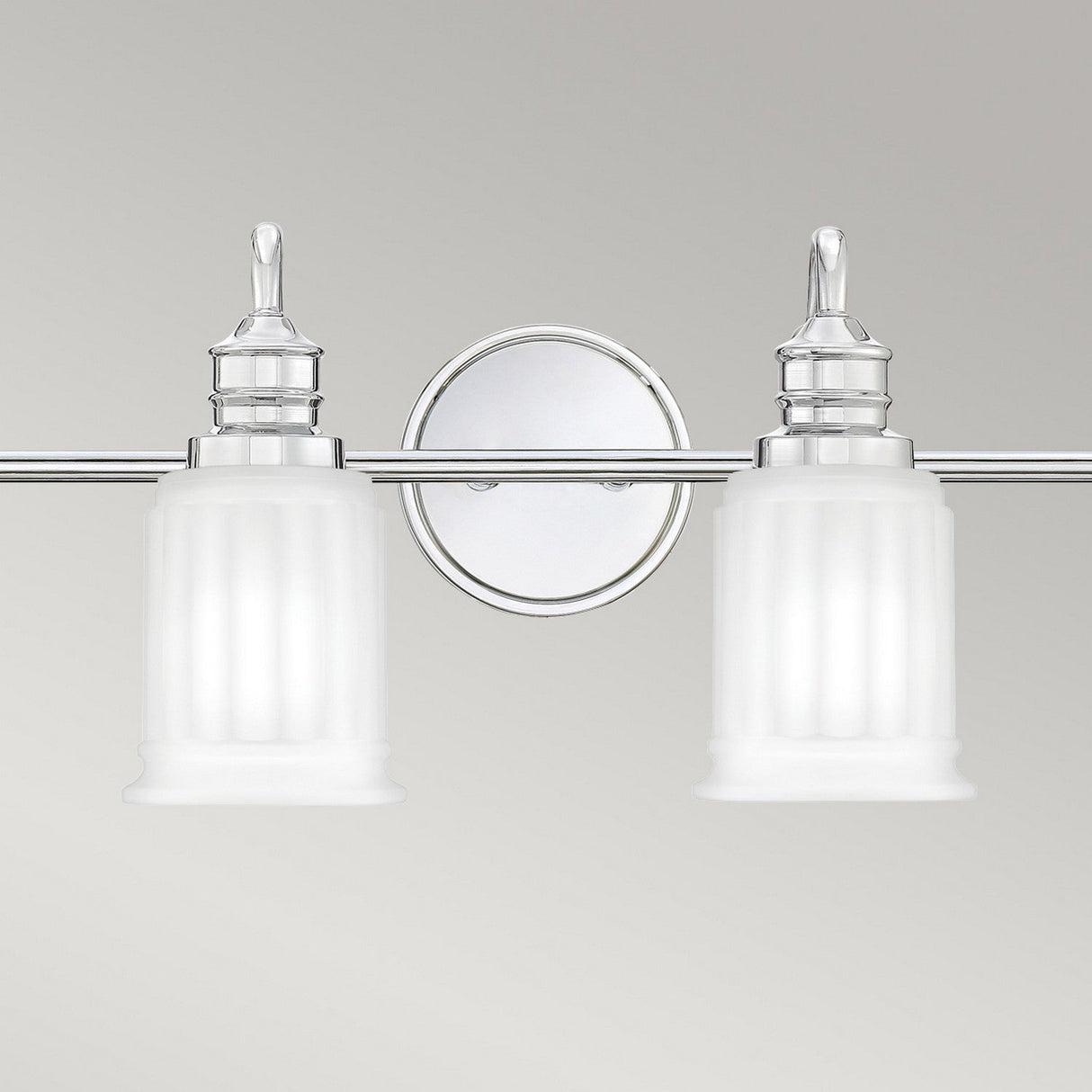 The Swell 4 Light Wall Light - Polished Chrome is presented against a neutral gray background, featuring two frosted glass shades. It's a sleek addition to modern home decor and an excellent choice for bathroom lighting.