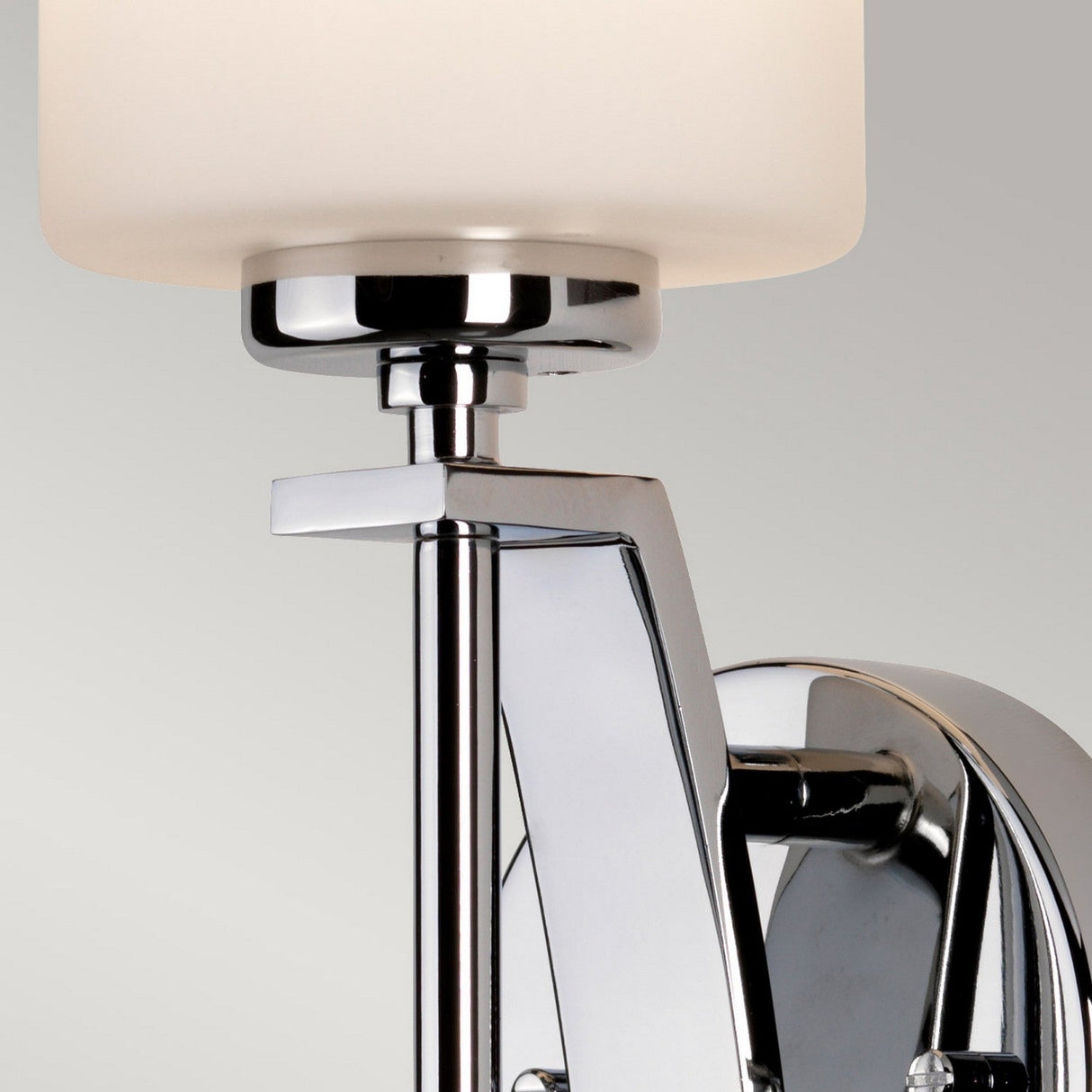 A close-up of the Taylor 1 Light Large Wall Light in polished chrome features an opal etched glass shade. The sleek, angular arm of this elegant modern fixture stands out against a light gray background.