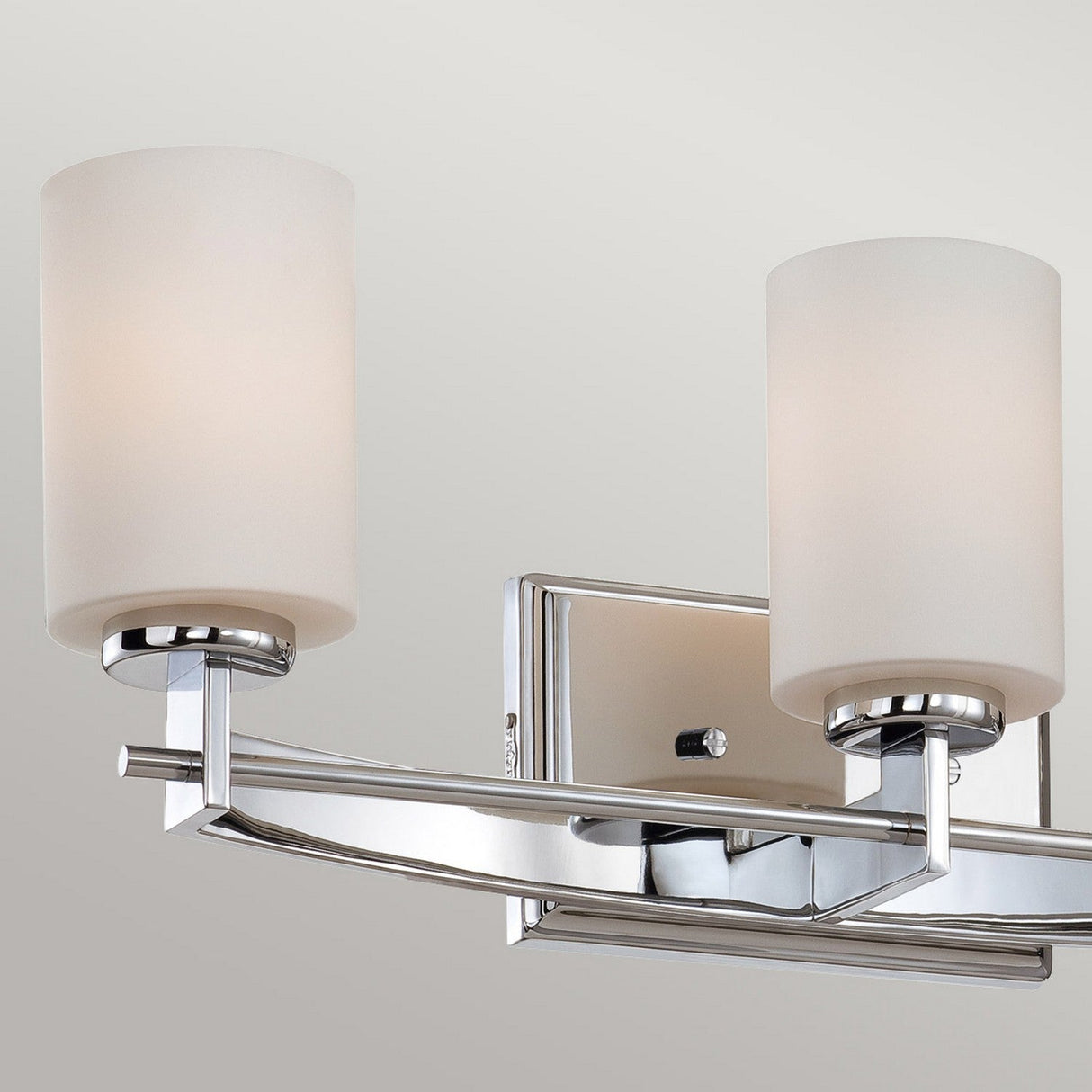 Introducing the Taylor 3 Light Wall Light - Polished Chrome, a contemporary wall-mounted fixture featuring two frosted glass cylindrical shades. This elegant light is finished in polished chrome and includes LED G9 bulbs. With an IP44 rating, it is mounted on a rectangular metal base, providing a soft, warm glow against any neutral background.