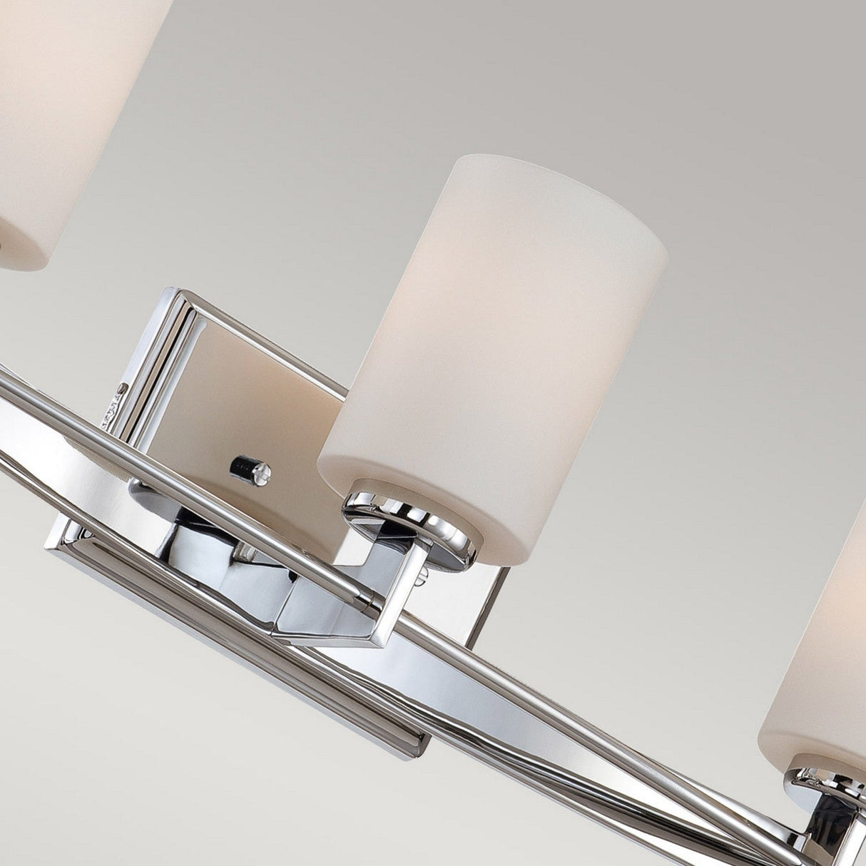 A close-up of the Taylor 3 Light Wall Light in polished chrome, showcasing its modern design with three cylindrical white frosted glass shades on a rectangular metal base. Compatible with energy-efficient LED G9 bulbs, it's set against a light gray background.