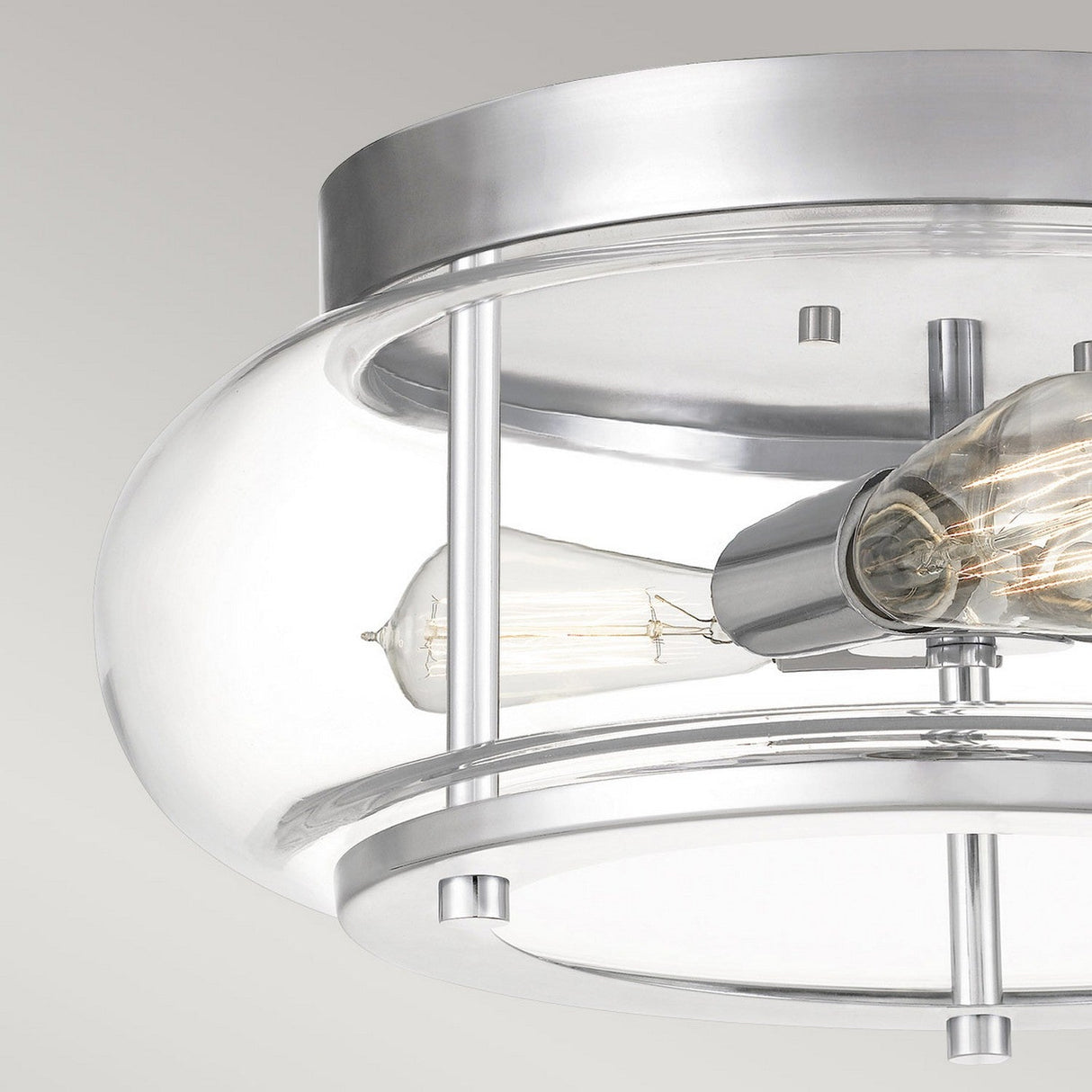 A close-up view of the Trilogy 3 Light Flush in polished chrome, showcasing its modern design with a clear glass dome and visible Edison bulb against a neutral background. The sleek metal frame enhances its sophisticated appearance.