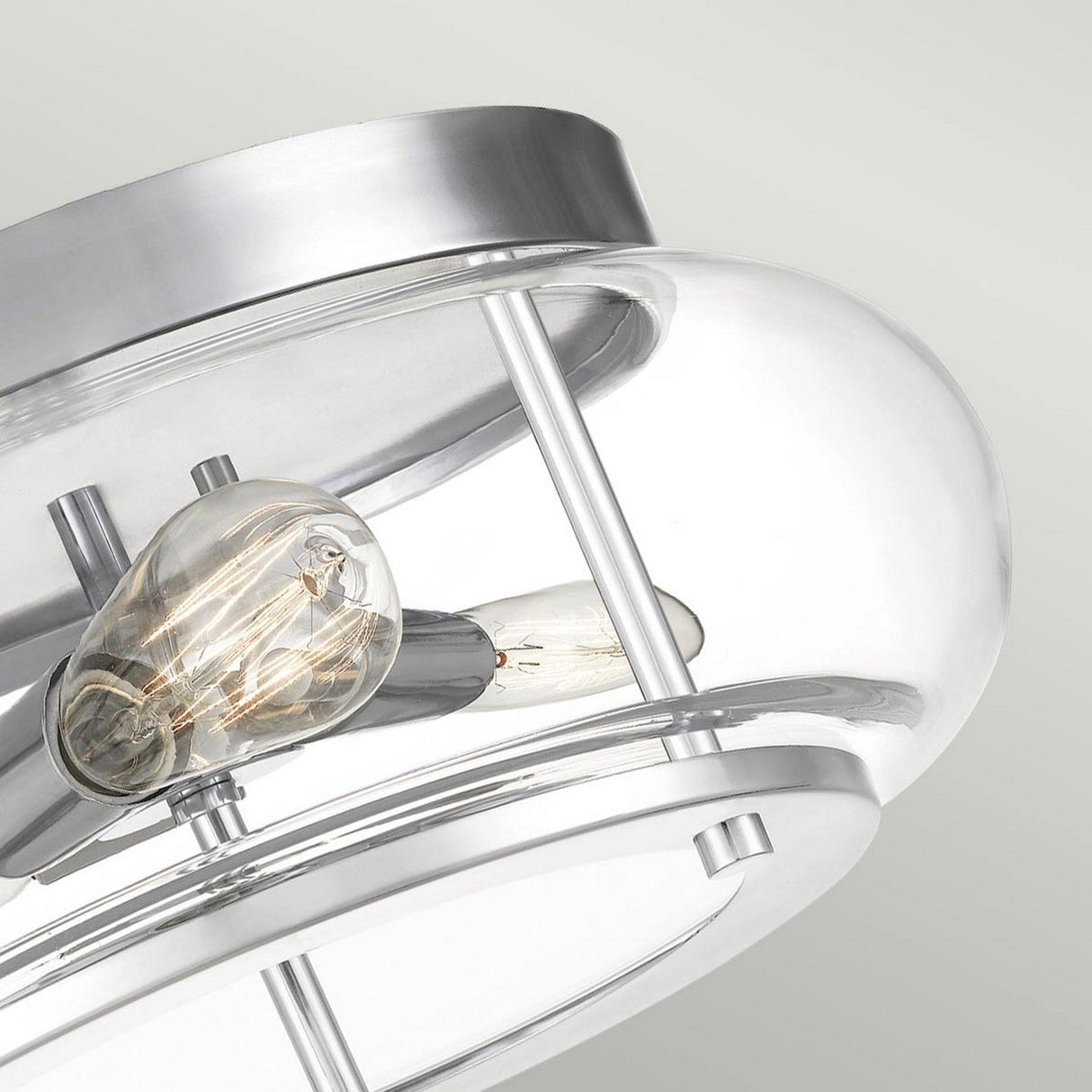 Close-up of the Trilogy 3 Light Flush in polished chrome, featuring a clear glass cover that reveals a visible bulb. The sleek flush mount design is elegantly displayed against a white ceiling.
