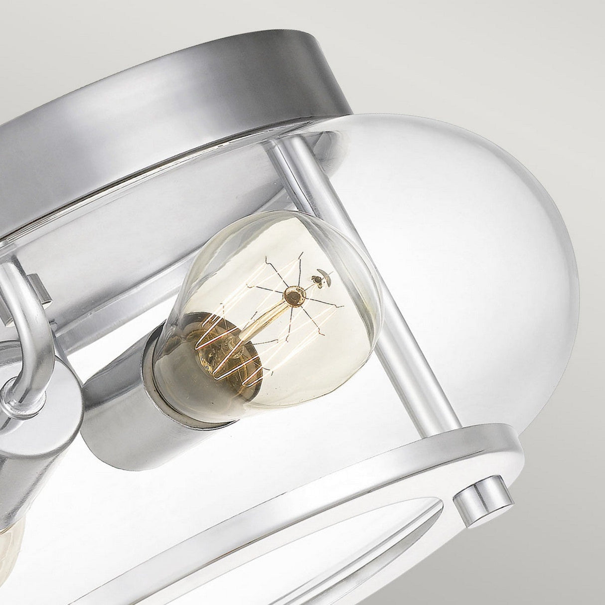 Close-up of the Trilogy 2 Light Flush in polished chrome, showcasing a visible filament bulb encased in seeded glass. This modern fixture features sleek, curved metal elements with a minimalist aesthetic set against a neutral background.