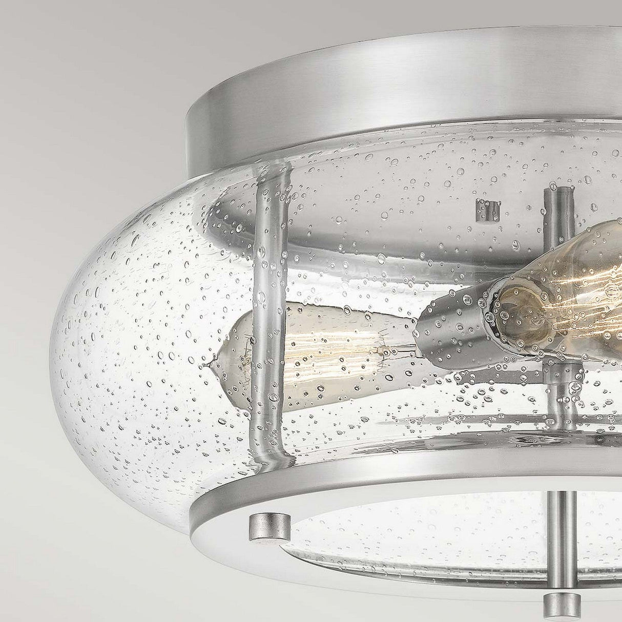 Close-up of the Trilogy 3 Light Flush in brushed nickel, featuring a clear, bubble-patterned glass shade. Inside, two visible Edison-style LED bulbs are mounted on metal rods, offering a modern and industrial aesthetic.