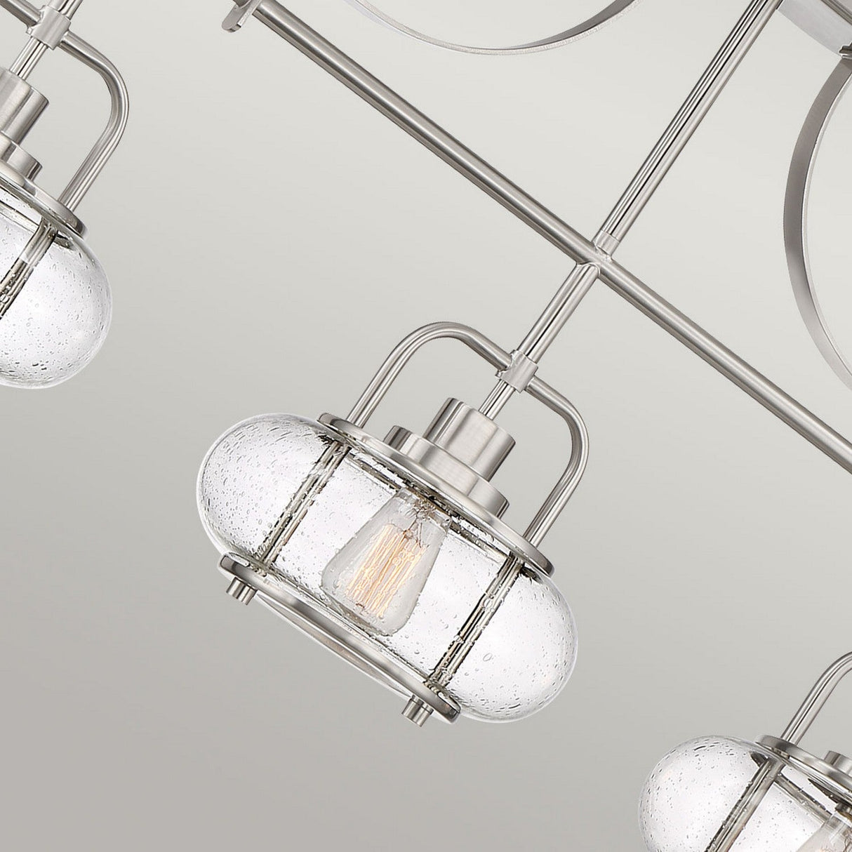 Close-up of the Trilogy 3 Light Island Light in brushed nickel, showcasing round seeded glass shades that encase filament bulbs, supported by sleek metal rods set against a neutral background.