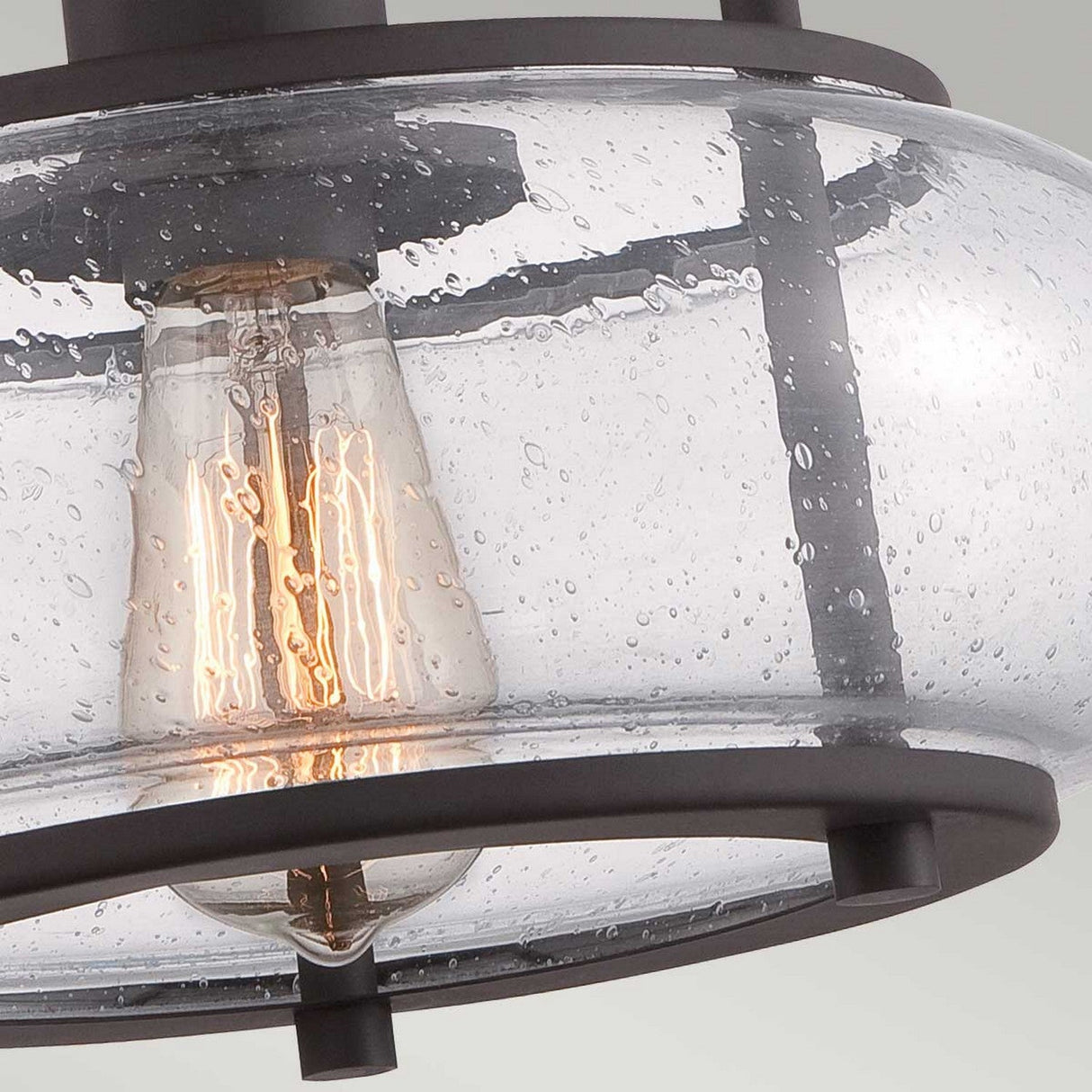 Close-up of the Trilogy 1 Light Small Semi-Flush featuring an Edison-style LED filament bulb inside a rounded, seeded glass shade. The glass has a textured, bubbly appearance, and the fixture is elegantly framed in Old Bronze metal.