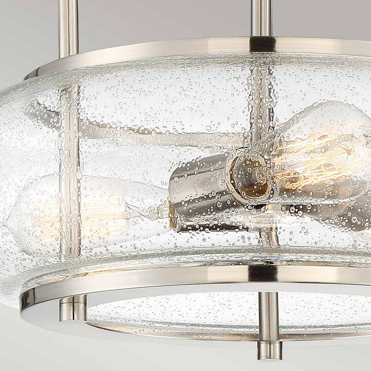 Close-up of the Trilogy 3 Light Semi-Flush - Brushed Nickel fixture, featuring three exposed LED filament bulbs. The design includes a round seeded glass shade and a brushed nickel frame, epitomizing an industrial aesthetic.