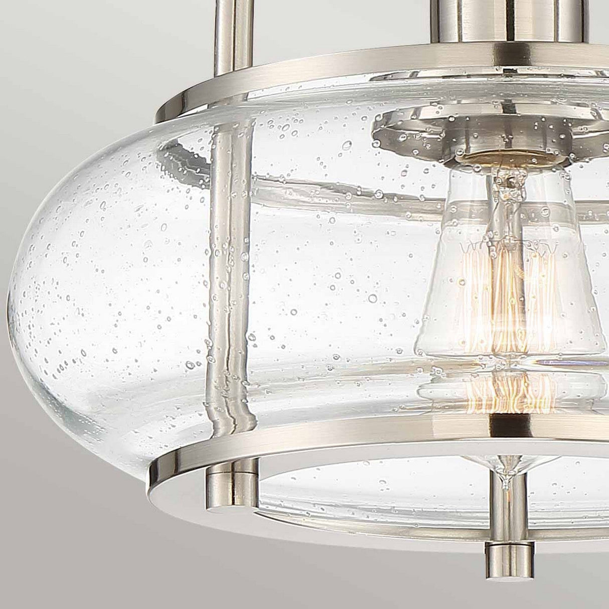 A close-up of the Trilogy 1 Light Semi-Flush in brushed nickel, featuring a modern ceiling light fixture with a clear seeded glass shade that boasts a bubble texture and highlights an exposed Edison bulb inside.