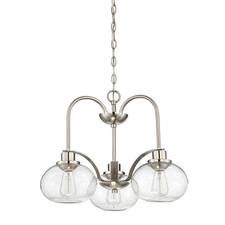 The Trilogy 3 Light Chandelier - Brushed Nickel features a contemporary design with three curved metallic arms, each holding a round seeded glass shade. The semi-flush fixture is suspended by a chain, with each shade encasing a visible light bulb for an elegant and modern look.