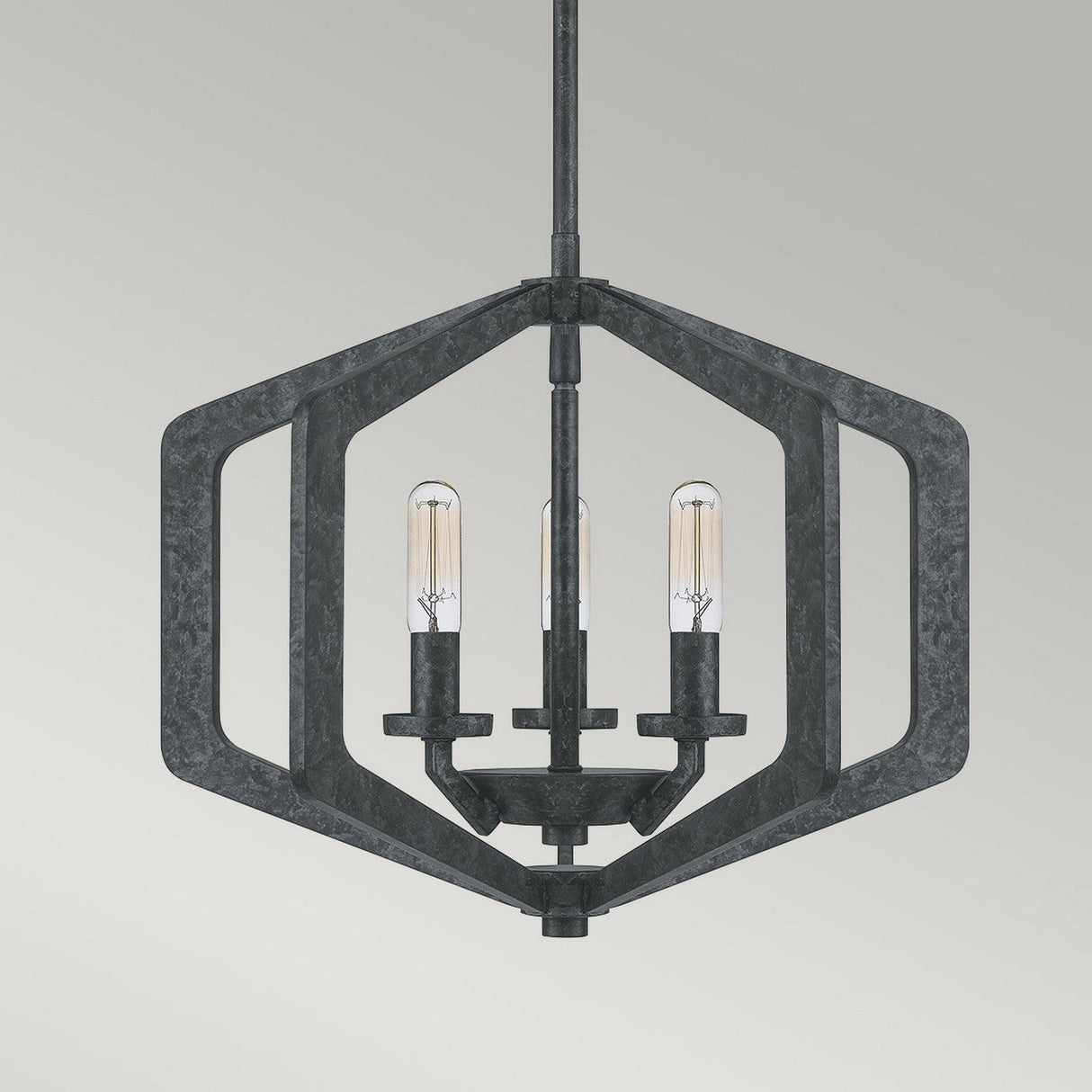 The Vanguard 3 Light Chandelier - Old Black is a modern, industrial-inspired fixture featuring a hexagonal metal frame in a sleek black finish, with three exposed light bulbs hanging elegantly against a neutral background.