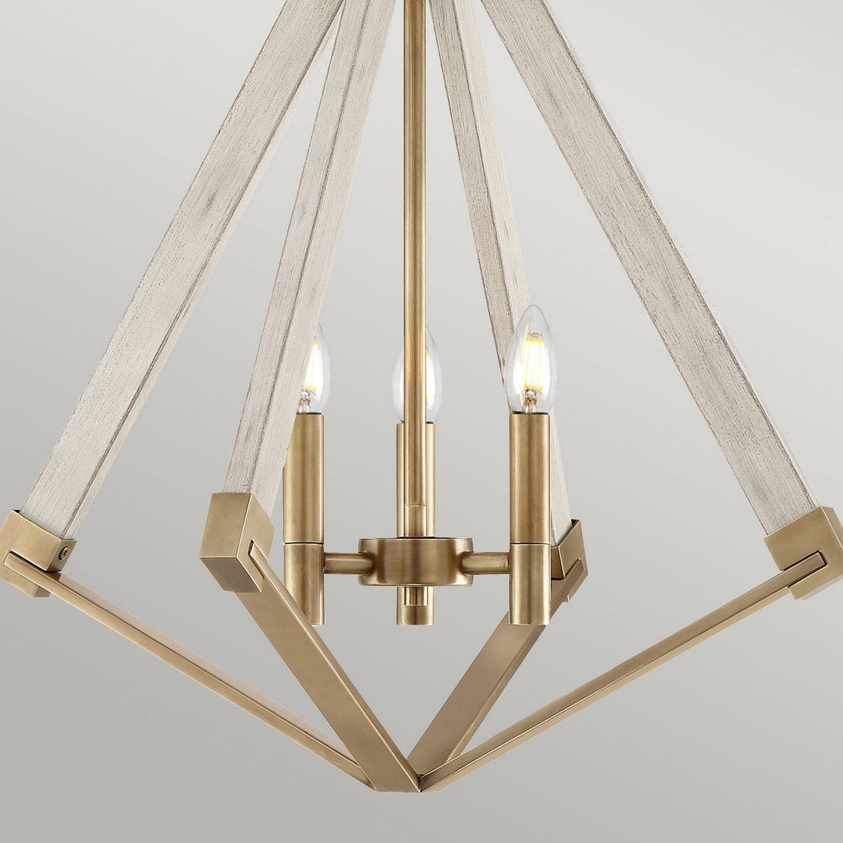The View Point 3 Light Chandelier showcases a modern farmhouse style with its geometric design, featuring a gold metal frame complemented by wooden and weathered brass accents. The chandelier elegantly displays three exposed light bulbs, creating a stunning effect against a neutral backdrop.