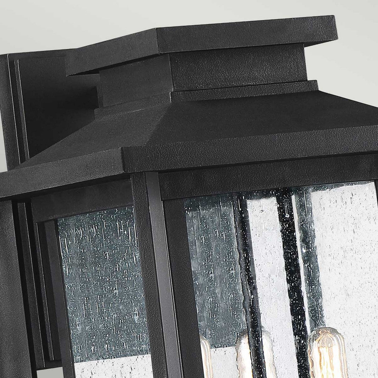 Close-up of the Wakefield Outdoor 3 Light Large Wall Lantern in earth black, featuring clear textured glass panels. The lantern's arts and crafts style is evident in its traditional rectangular shape, showcasing two vintage-style filament bulbs within the slightly wavy glass.