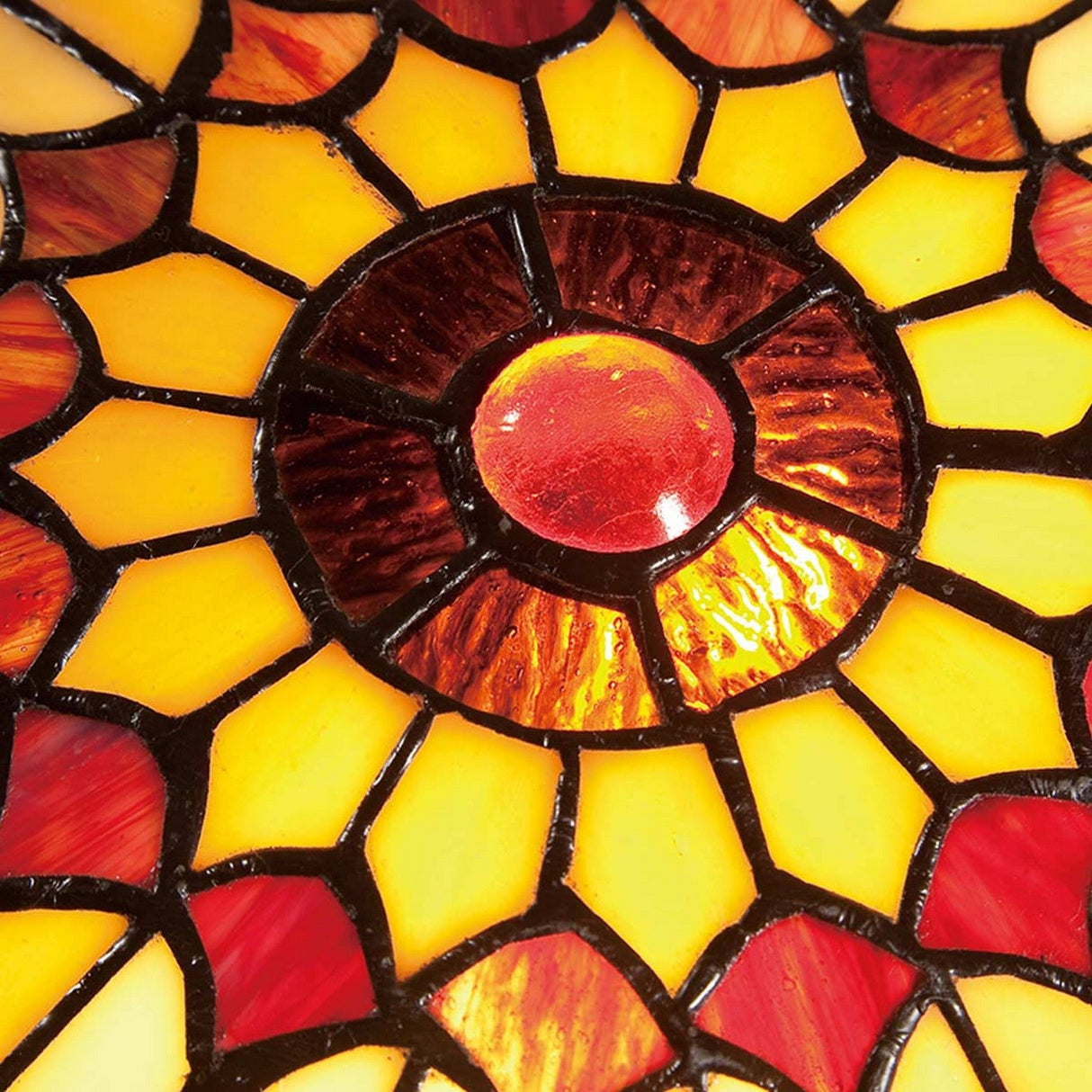 The West End 2 Light Medium Floating Tiffany Flush in Vintage Bronze showcases a detailed Tiffany-style stained glass design. It features a circular pattern with shades of red, orange, and yellow, where the central red circle is encircled by petal-like segments arranged in a sunburst style. The vintage bronze framing enhances its warm and vibrant appearance.