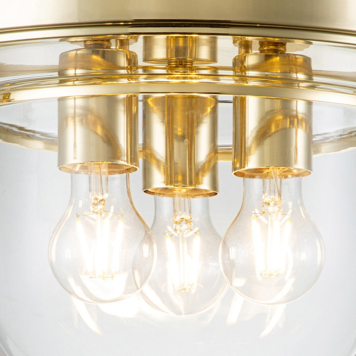Close-up view of the Whistling 3 Light Flush in polished brass, featuring three exposed light bulbs. Perfect for bathroom lighting, this IP44-rated fixture emits a warm glow and boasts a modern, elegant design.