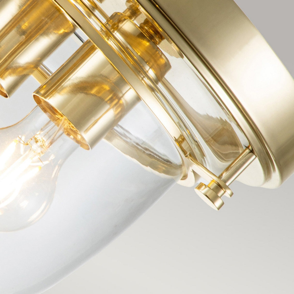 Close-up of the Whistling 3 Light Flush - Polished Brass ceiling light fixture, featuring polished brass and glass elements in bathroom lighting with exposed bulbs. The illuminated bulbs enhance its modern, sleek design as the brass components reflect a warm glow, accentuating its elegance.
