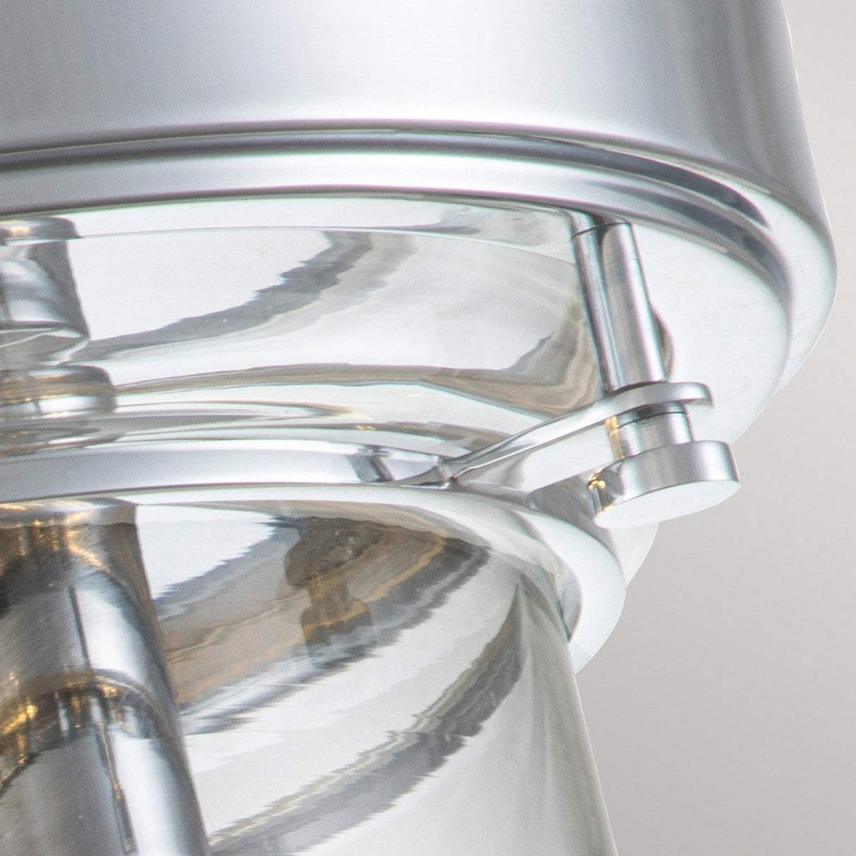 Close-up of the Whistling 3 Light Flush in polished chrome with a latch mechanism on a reflective, cylindrical base. The sleek surface highlights a modern design, capturing light and reflections beautifully.