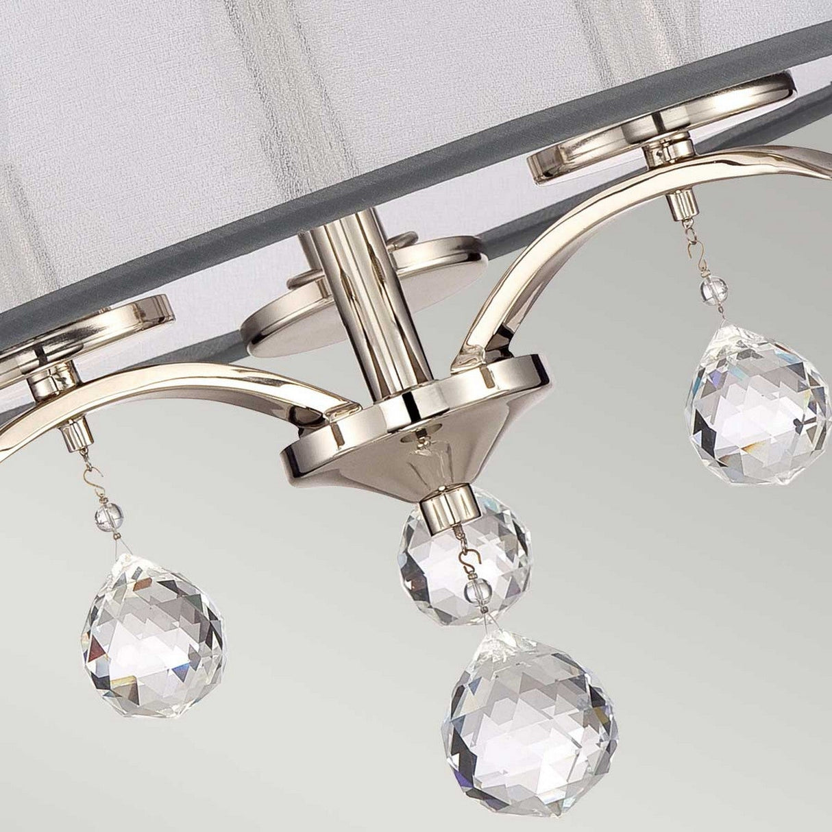 A close-up of the Whitney 3 Light Semi-Flush in Imperial Silver reveals its graceful design, featuring three crystal teardrops. The crystal accents beautifully reflect light through their intricate cuts, adding an elegant touch beneath the white fabric shade.