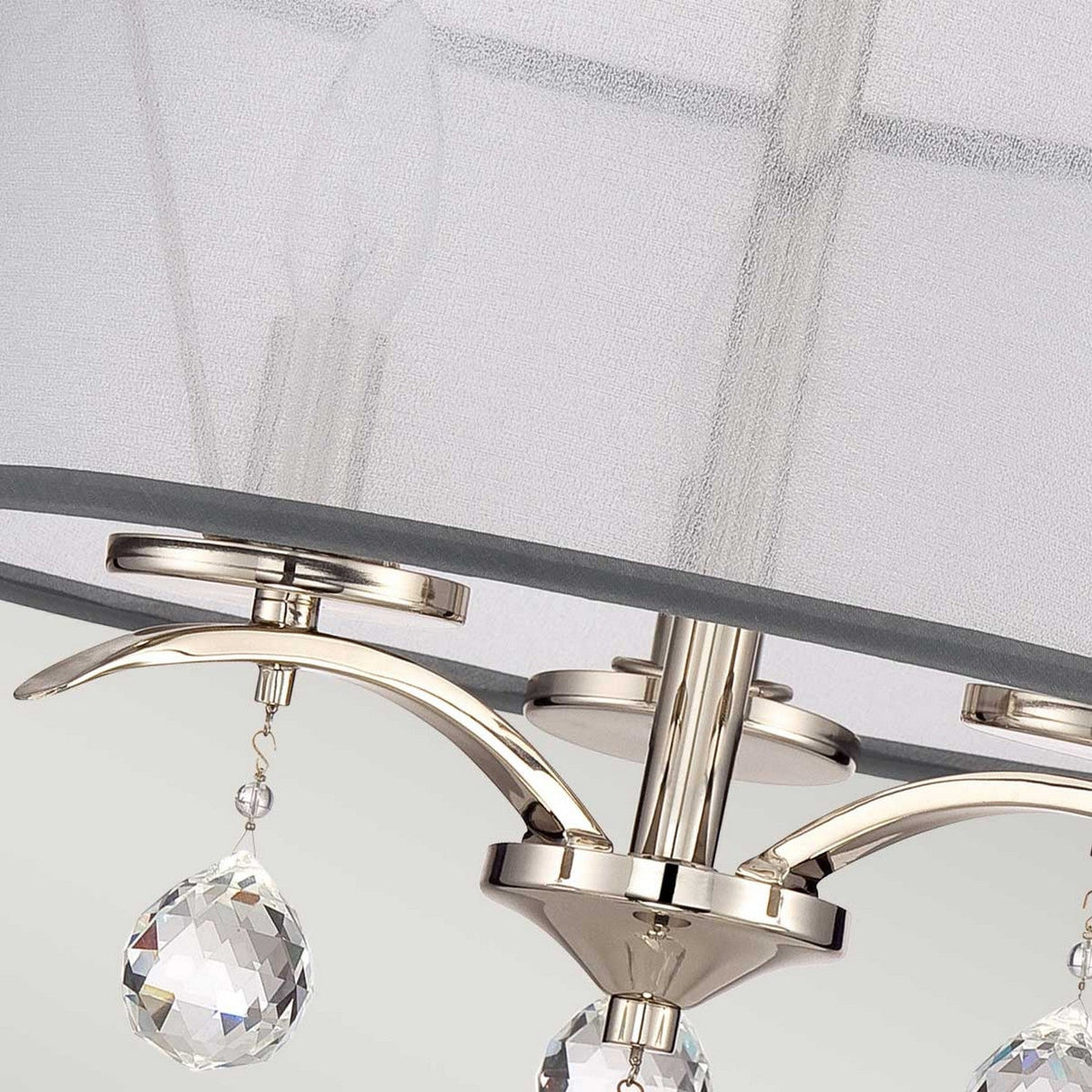 This close-up of the Whitney 3 Light Semi-Flush - Imperial Silver showcases its modern chandelier design with an Imperial Silver finish and clear teardrop crystal accents. The elegant arrangement features two visible bulbs adorned with an opaque white shade, adding a soft touch to its sophisticated look.