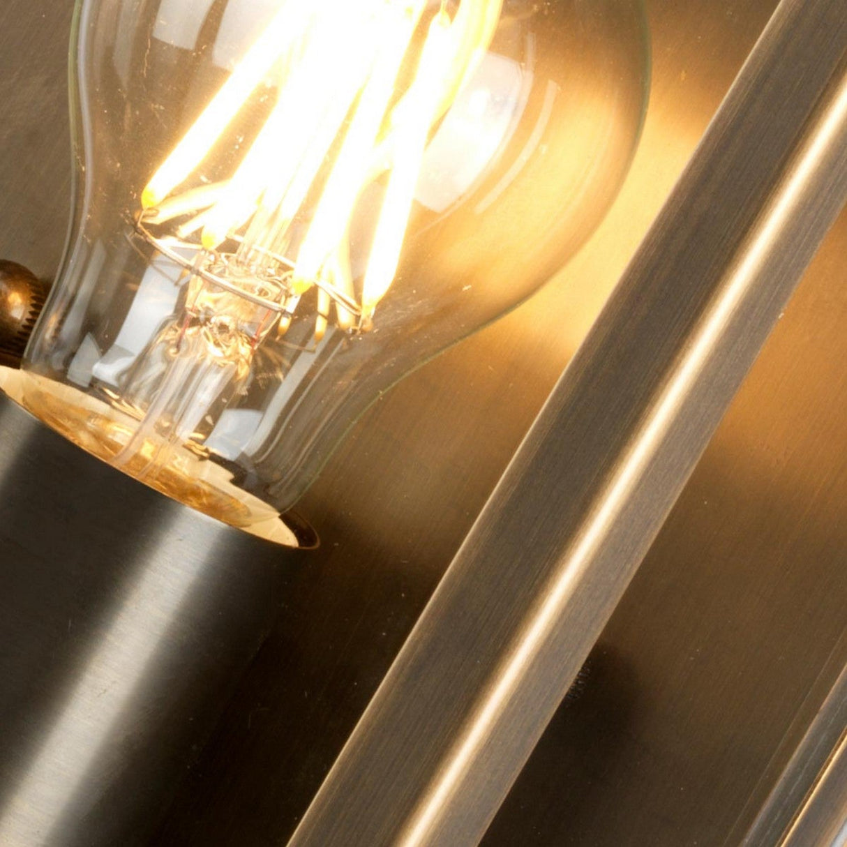 Close-up of the Regents Park 1 Light Outdoor Wall Light in aged brass, featuring an illuminated vintage-style bulb with exposed filaments. The warm glow contrasts against the smooth, reflective metal surface, creating a cozy atmosphere reminiscent of its IP44-rated design.