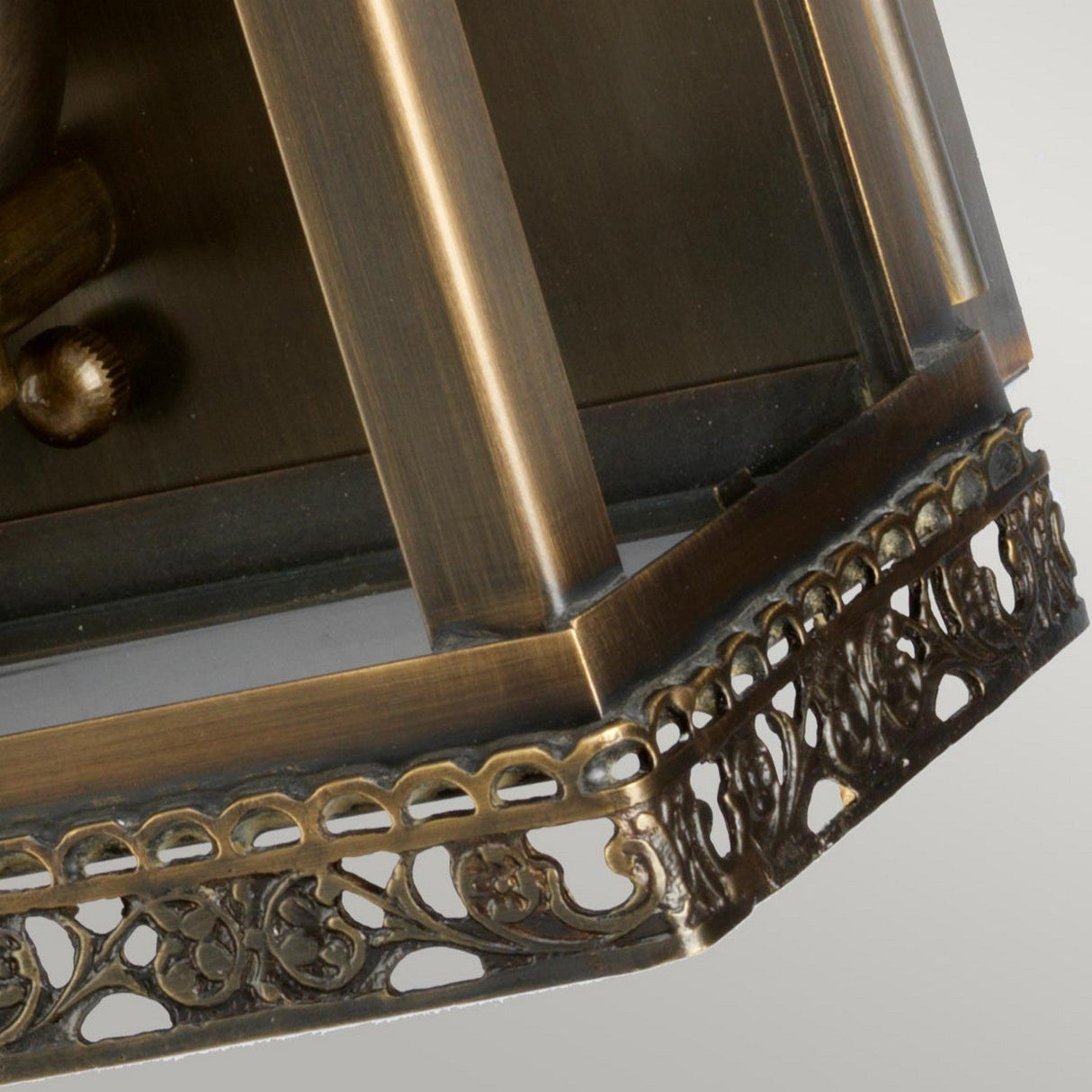 The Regents Park 1 Light Outdoor Wall Light in Aged Brass boasts a bronze-colored frame with intricate scrollwork and a glass pane, exuding the charm of vintage craftsmanship with its warm glow and IP44 weather-resistant rating.