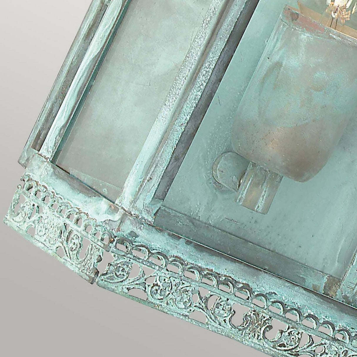 Close-up of the Regents Park 1 Light Outdoor Wall Light in Verdigris, showcasing its intricate metalwork and verdigris finish. The design includes a glass enclosure and partially visible bulb, contributing to its antique appearance against a gradient background.