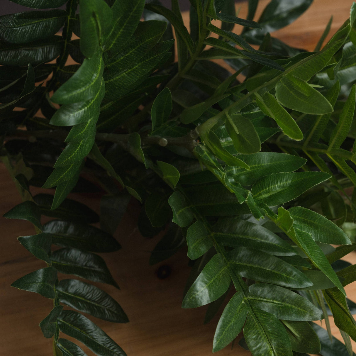 Close-up of the Hill Interiors Pistach Bunch faux foliage, showing clusters of glossy green pistachio-style leaves on slender stems against a wooden surface.