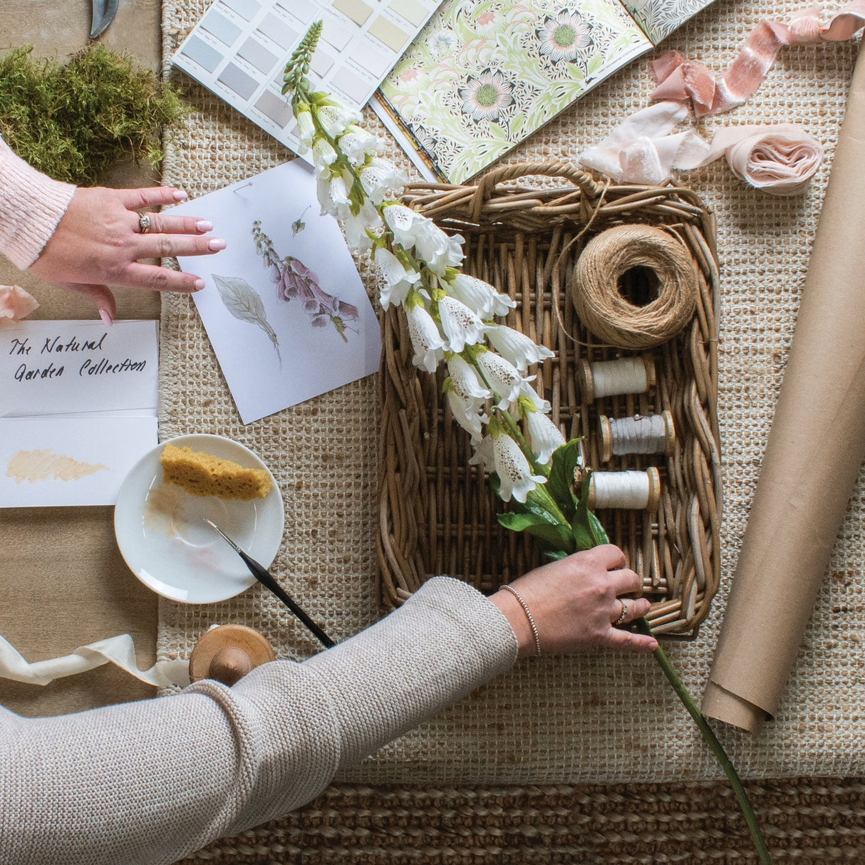 Hill Interiors White Foxglove faux stem with tall spires of speckled bell blooms, styled on a woven mat with wicker tray, twine and ribbons.