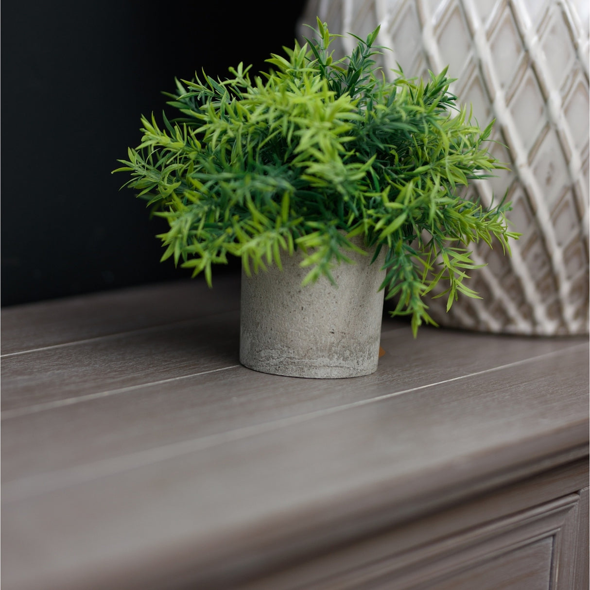 Hill Interiors small bamboo faux plant with slim green leaves in a grey pot, styled on a wooden surface beside a lattice-patterned vase.