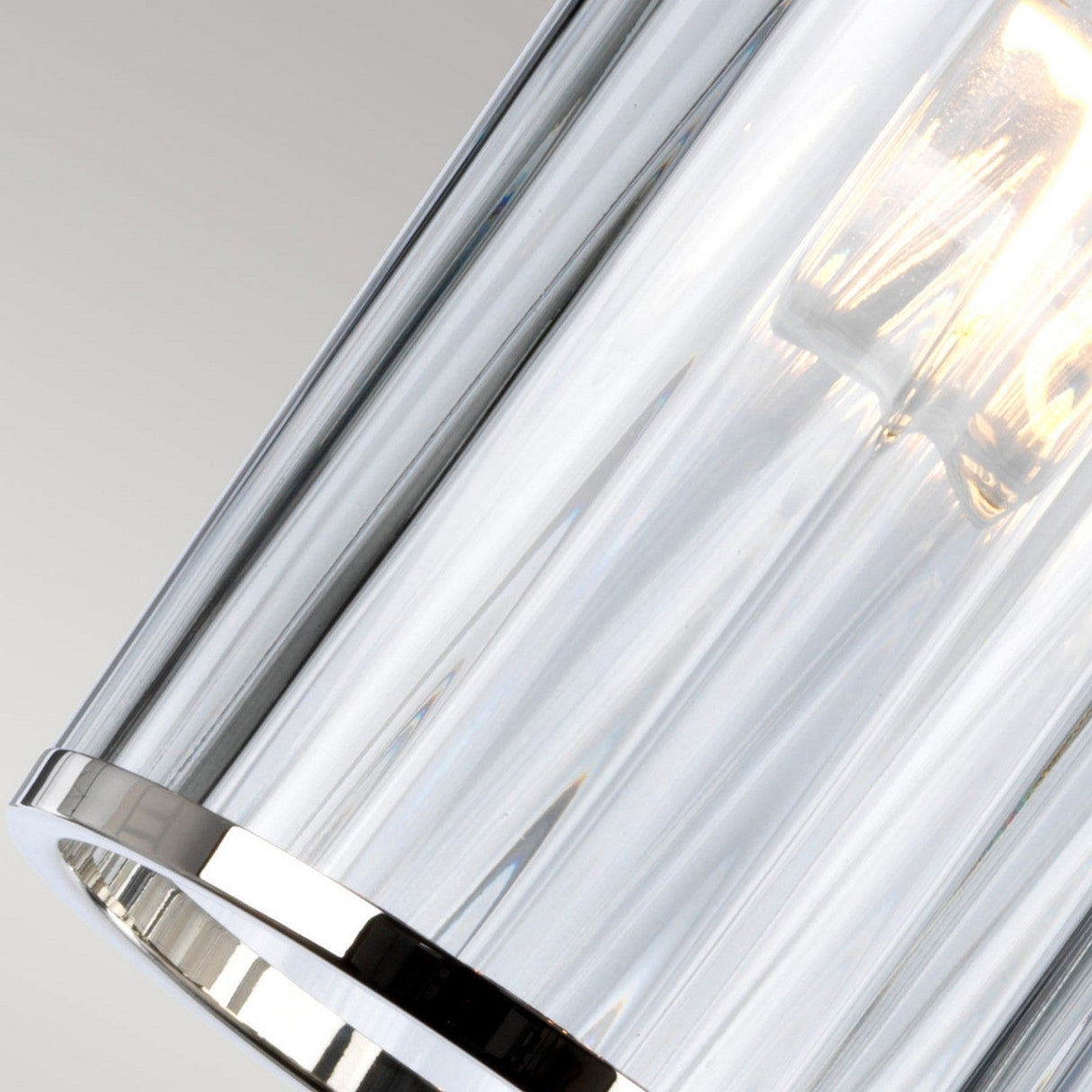 A close-up of the Reno 1 Light Pendant showcases its modern design with a sleek, cylindrical smoke glass shade complemented by polished nickel accents. The warm light bulb inside emits a soft glow, enhancing the elegant ambiance against a neutral background.
