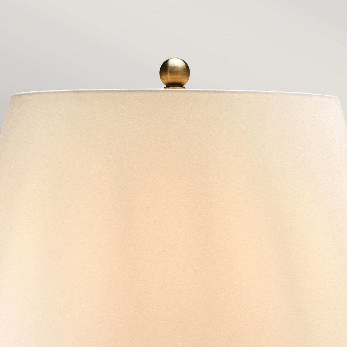 Close-up of the brown and black Rib Pumpkin 1 Light Table Lamp featuring a beige faux silk lampshade topped with a small, round brass finial. The ceramic base elegantly supports the shade against a neutral gray background.
