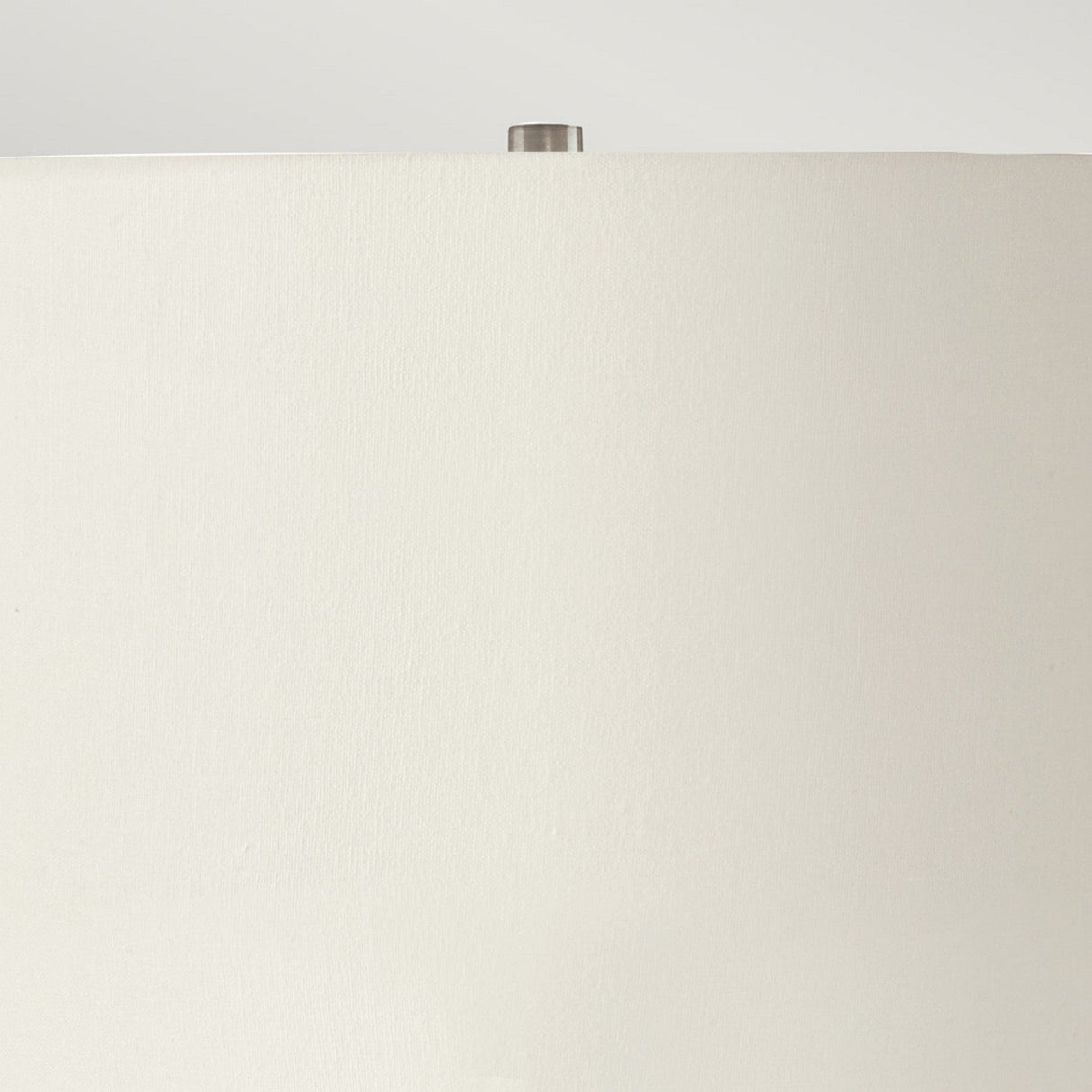 A close-up view showcases the Ripple 1 Light Table Lamp in black, featuring a white cylindrical lampshade topped with a small metallic finial. Its modern design contrasts beautifully against the light gray background, adding an element of striking decor to the space.