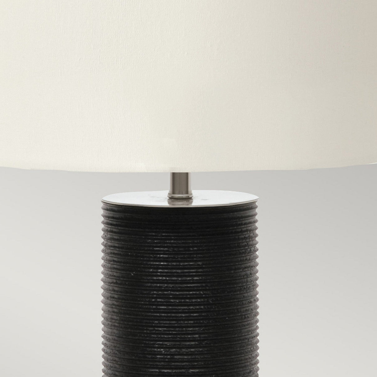 The Ripple 1 Light Table Lamp, featuring a sleek black base with a textured cylindrical design and topped with a smooth white shade, creates an elegant contrast in decor against a plain background.