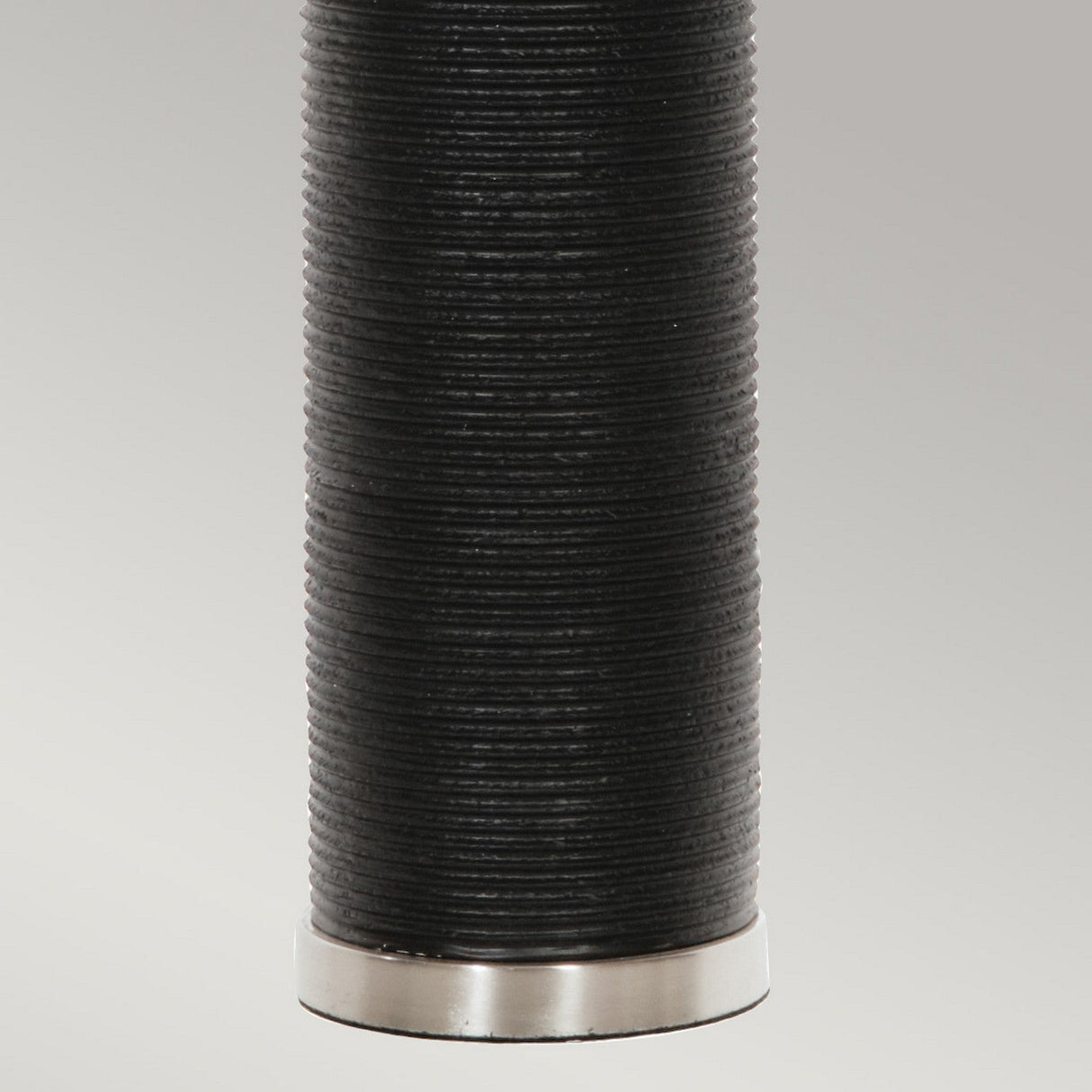Close-up of a dark, textured cylindrical object with a metal base against a plain background, embodying the essence of modern design. The Ripple 1 Light Table Lamp - Black With White Shade stands as a striking piece of contrast decor, effortlessly blending into any contemporary space.