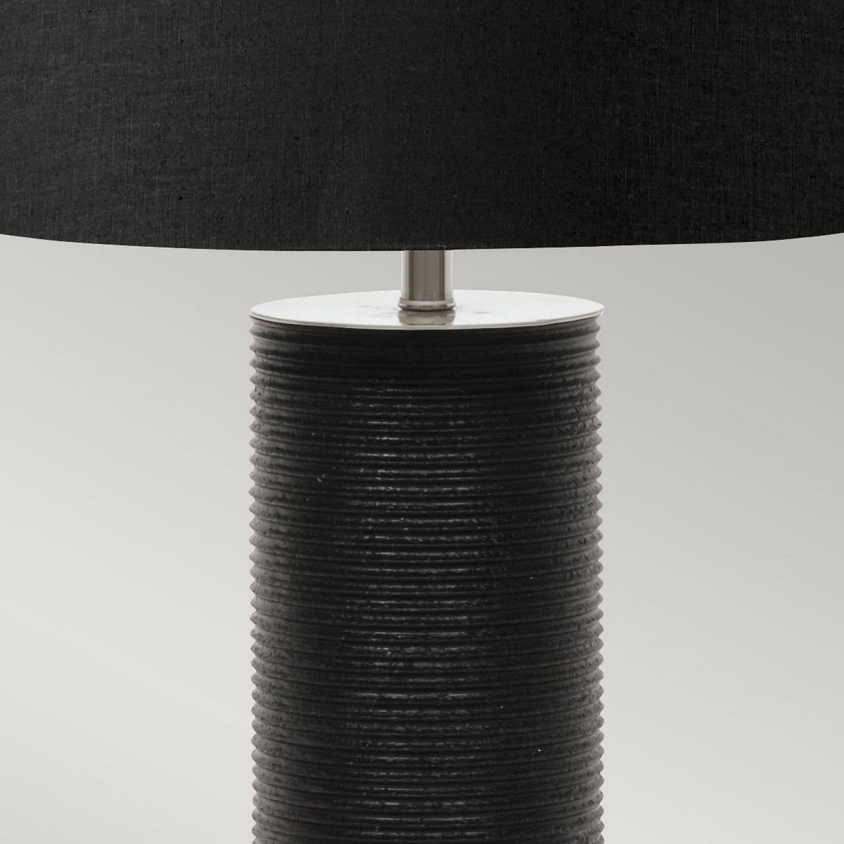A close-up of the Ripple 1 Light Table Lamp in black, showcasing its cylindrical textured base with horizontal grooves and a large lampshade against a neutral backdrop. This contemporary lighting piece boasts a minimalist design.