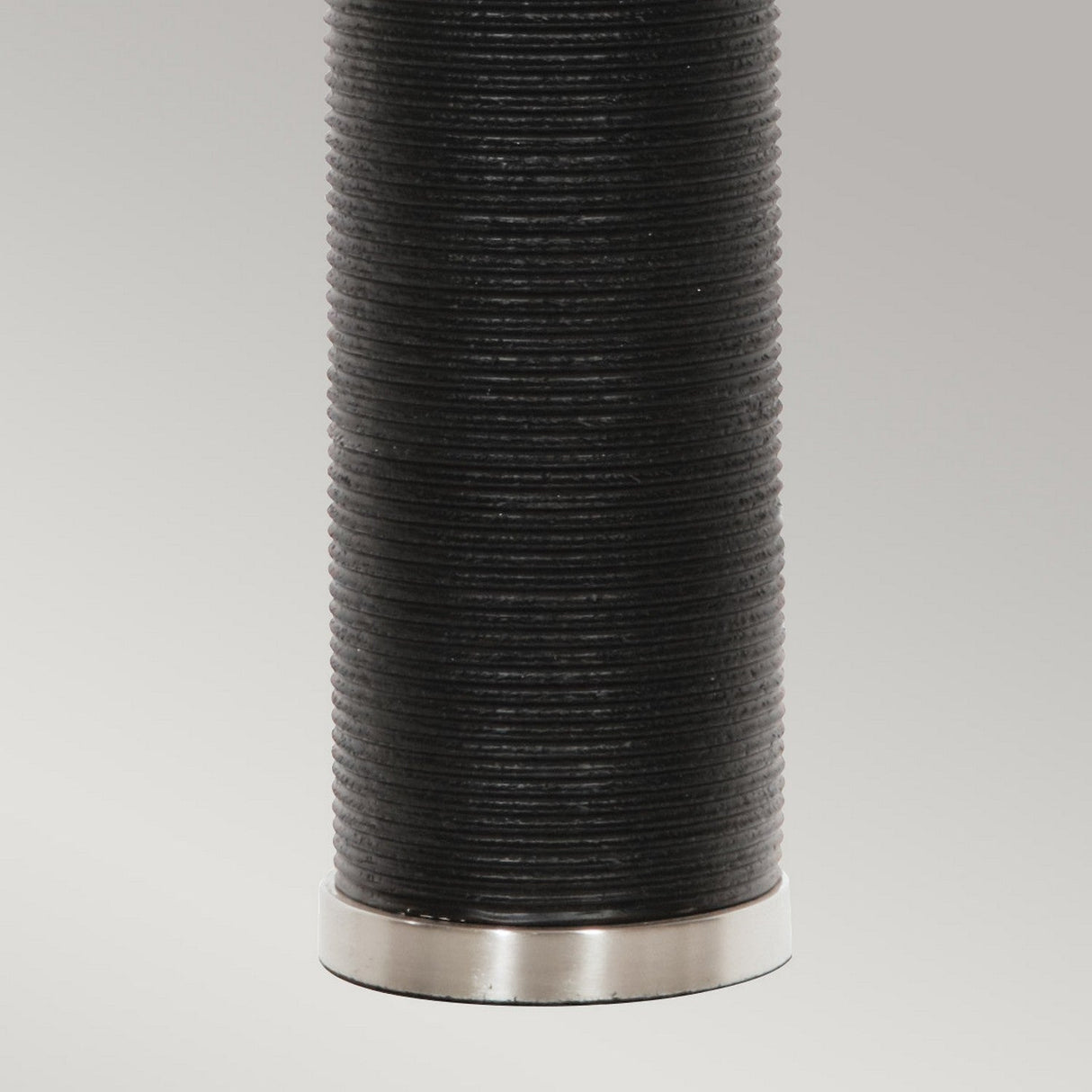 A close-up of the Ripple 1 Light Table Lamp, with its cylindrical design and black shade, complements the minimalist decor. The base is accented with a silver metal rim. A plain light grey background highlights its contemporary aesthetic.