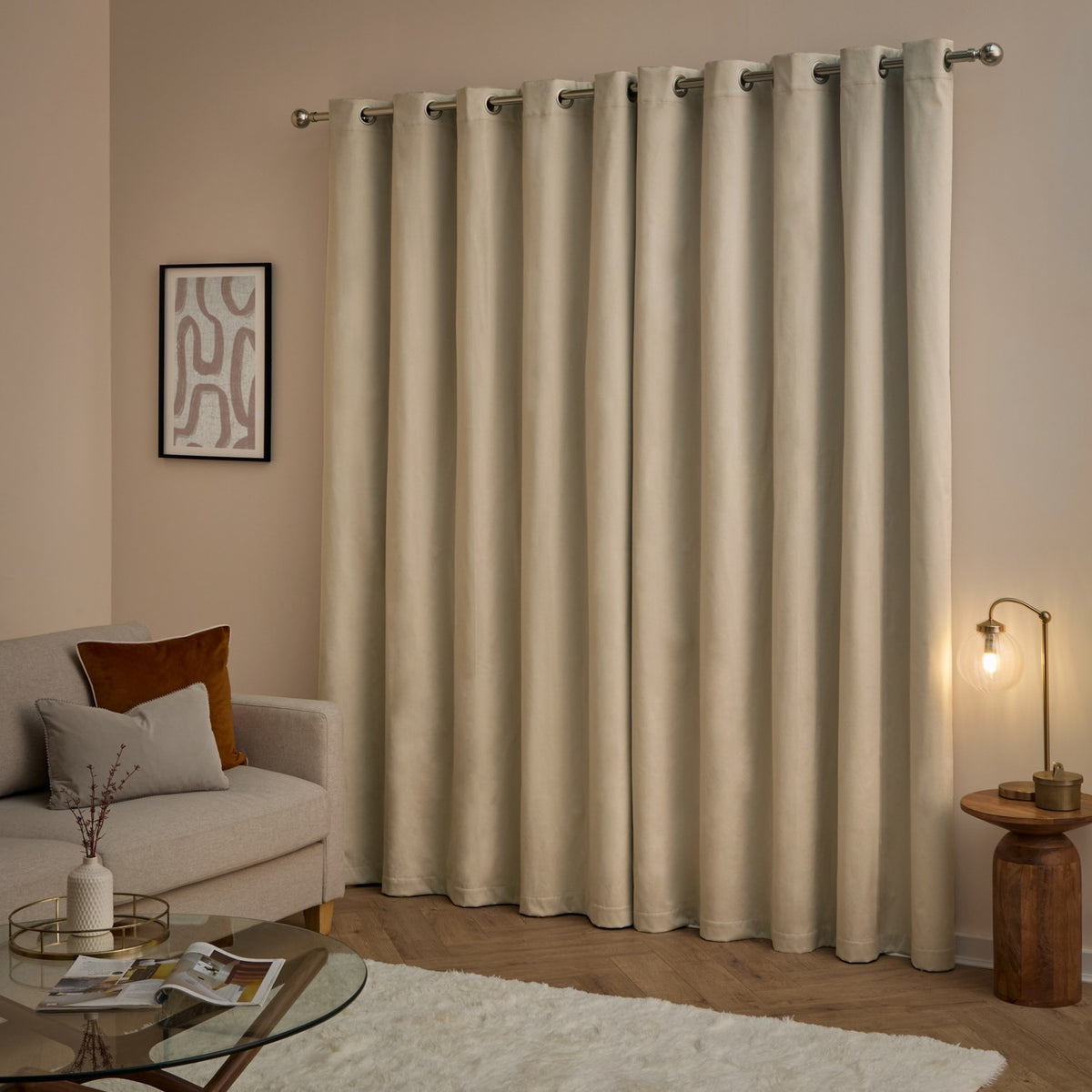 Natural velvet eyelet curtains hanging on a brushed metal pole in a living room, styled with soft ambient lighting near a sofa and side table.