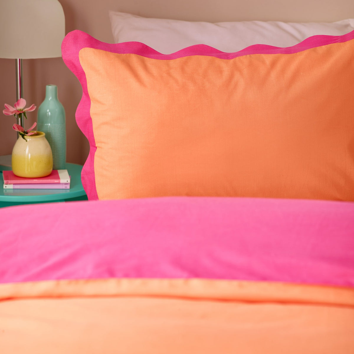 Wiggle Scallop duvet cover set on a bed, showing coral orange and vivid pink cotton-blend fabric with a scalloped pink trim, styled with a matching pillowcase in a bedroom setting.