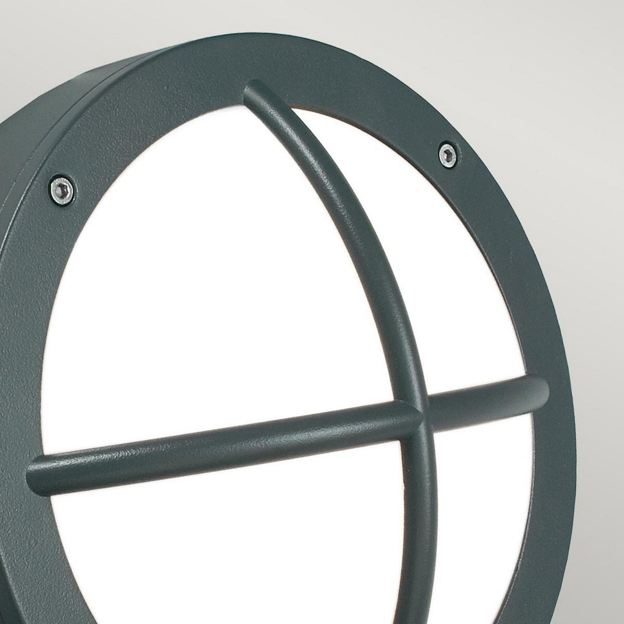 Close-up of the Rondane Outdoor LED Wall Light - Graphite featuring a round design with a black metal frame and two crossbars overlaying a white light diffuser. This energy-efficient lighting design includes a matte finish, visible screws for secure installation, and an IP65 rating for exceptional weather resistance.