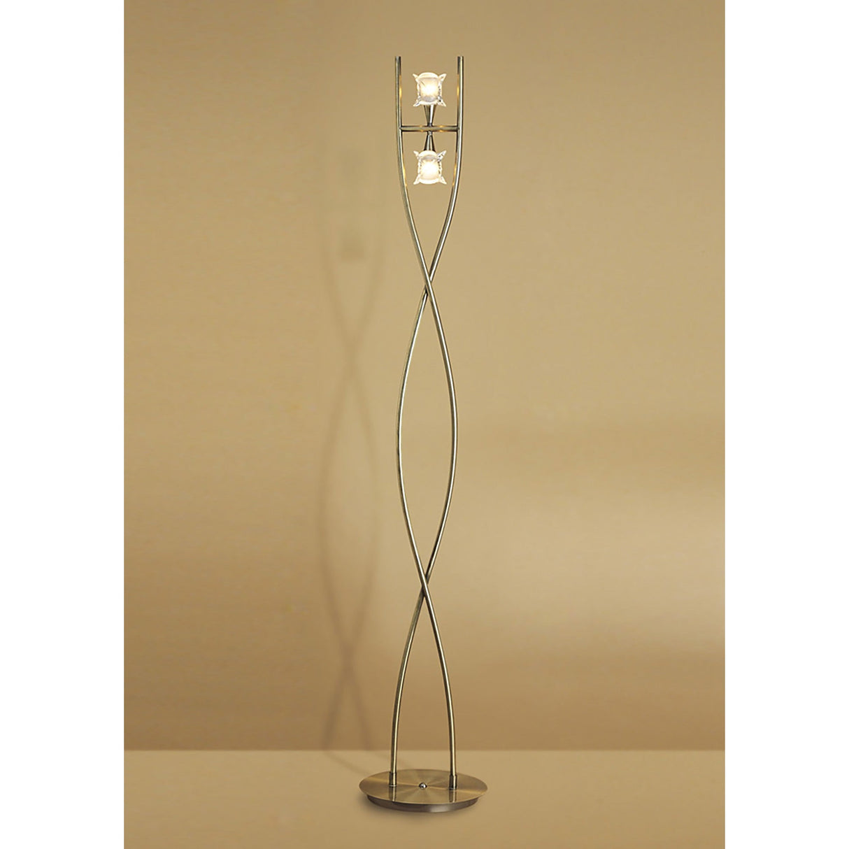 The Rosa Del Desierto 2 Light Floor Lamp in antique brass features a twisted metal frame, modern glass shades, and two exposed bulbs on a round base, providing elegant ambient lighting against any beige wall.