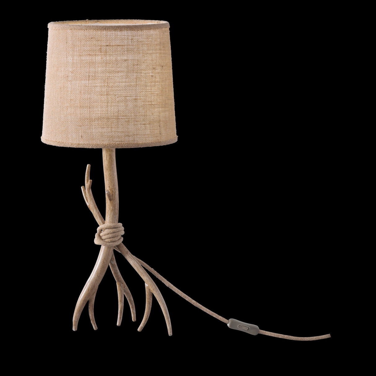 The Sabina 1 Light Table Lamp features a rustic brown base resembling intertwined antlers and a linen shade. The visible power cord and switch extend from the lamp, all set against a black background.