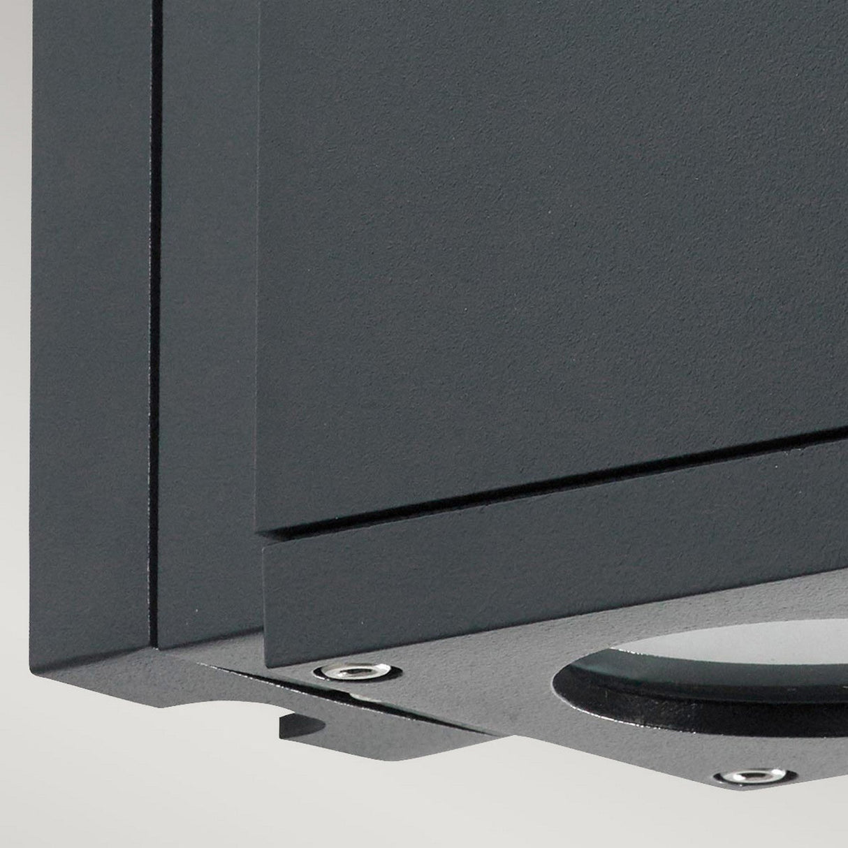 Close-up of a dark grey metal corner featuring visible bolts and a curved plate at the base, all showcasing a smooth, matte graphite finish. Perfect for the Sandvik Outdoor 1 Light Down Wall Light, which is IP65-rated for outdoor use.