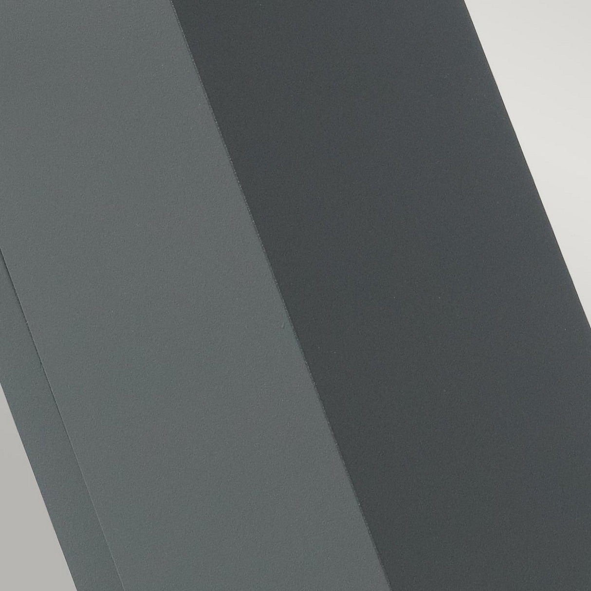 Close-up of two intersecting rectangular surfaces, one dark gray and the other light gray, forming an angular structure reminiscent of the Sandvik Outdoor 2 Light Up & Down Wall Light - Graphite. The graphite finish highlights their smooth texture and clean lines, creating a minimalist and abstract composition.