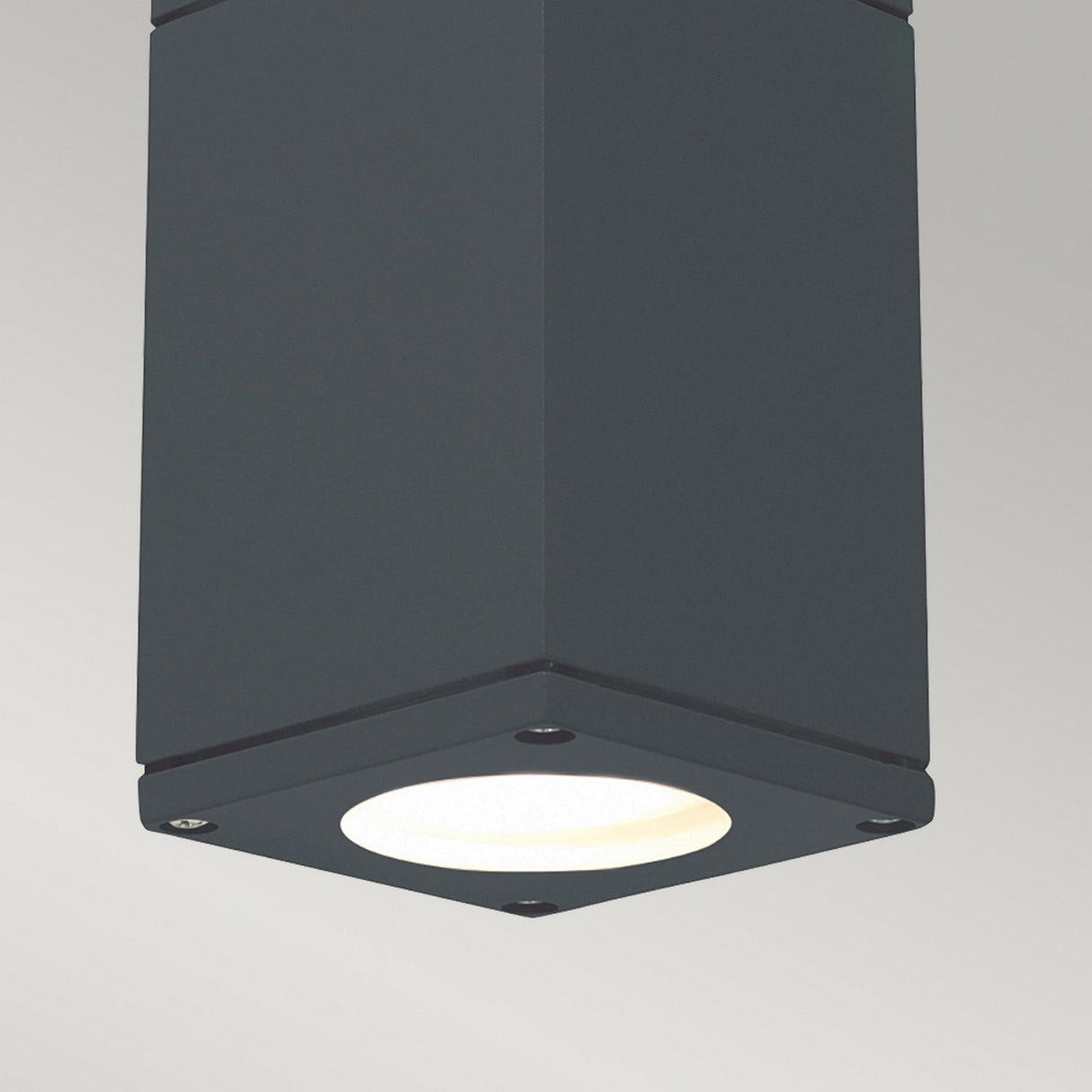 The Sandvik Outdoor 1 Light Down Ceiling Light - Graphite boasts a sleek, modern square design with its graphite finish and contrasts beautifully with the bright white bulb. It features an IP65 rating, ensuring it can endure various weather conditions while delivering dependable illumination against a light gray background.